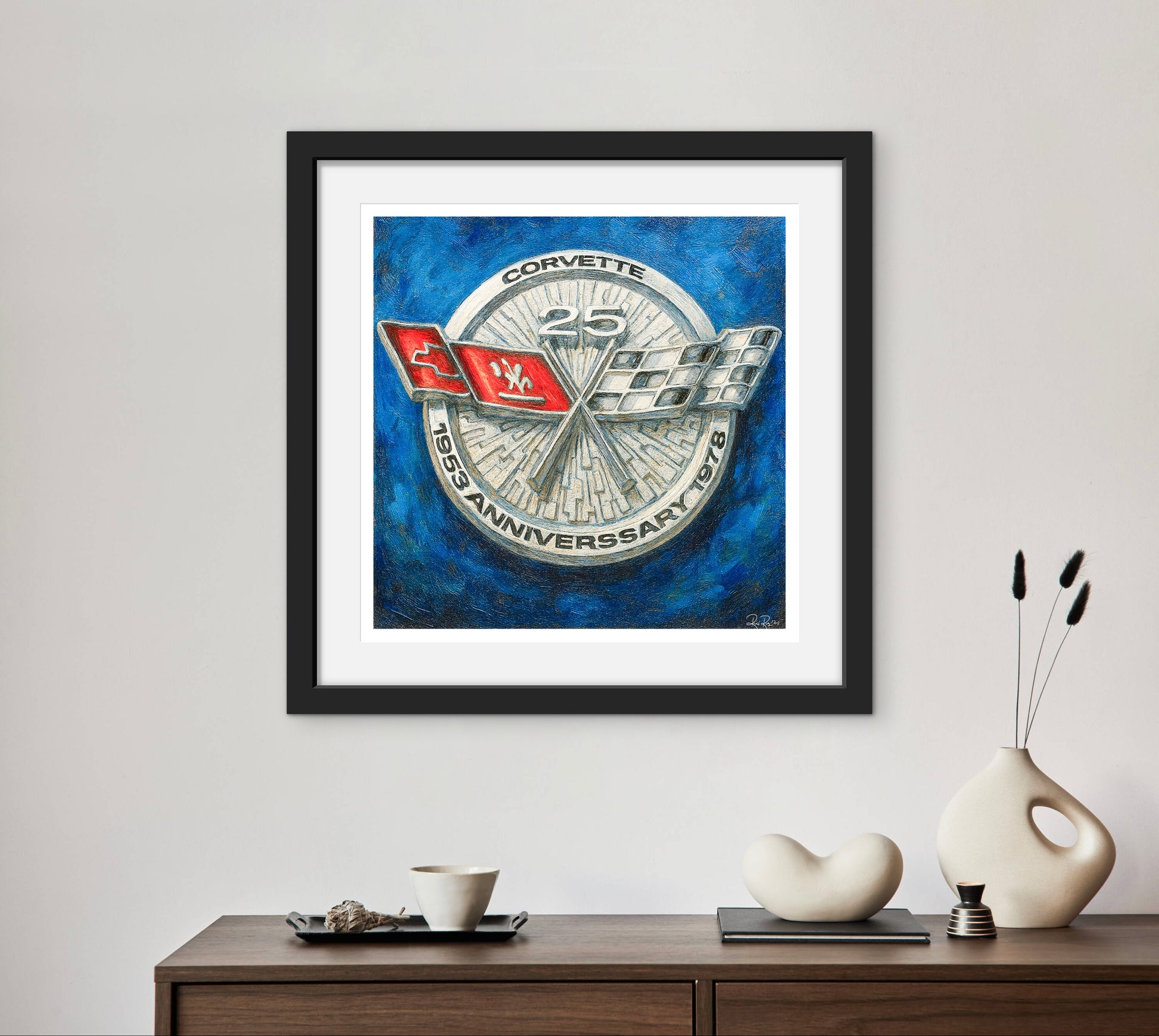 Framed Corvette logo art piece on a wall above a wooden console table with decorative items.