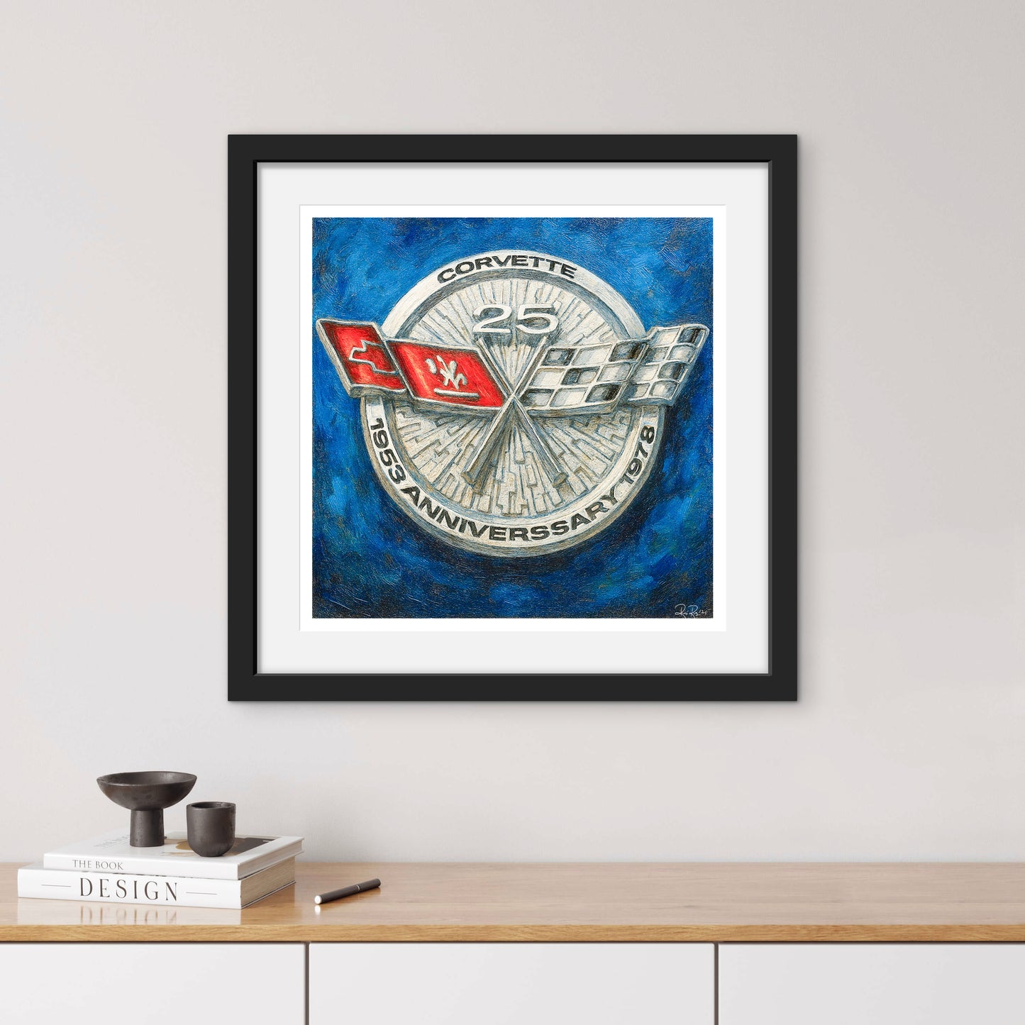 Framed artwork of a Corvette logo on a blue background, displayed on a wall above a wooden shelf.