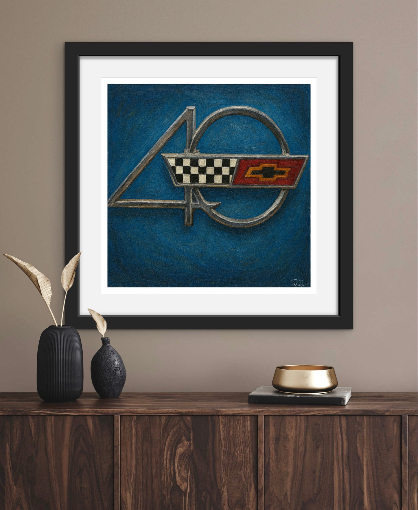 Framed artwork of a car emblem on a wall above a wooden console table.