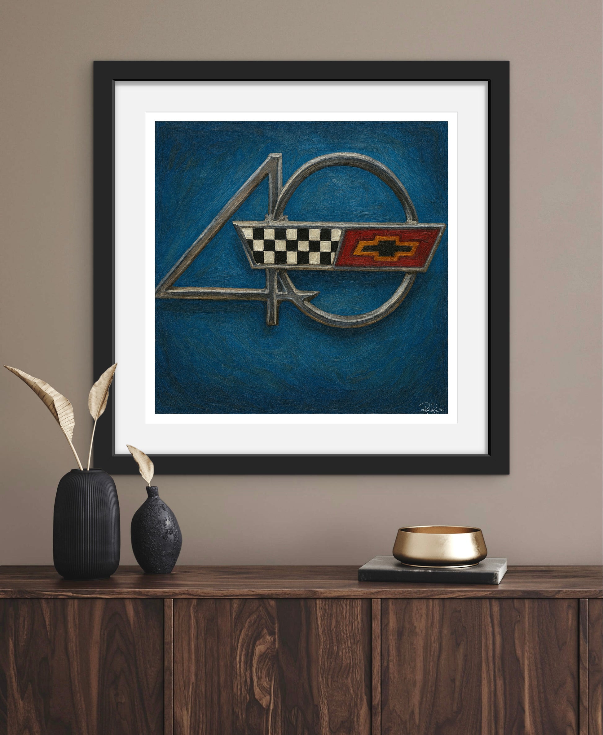 Framed artwork of a car emblem on a wall above a wooden console table.