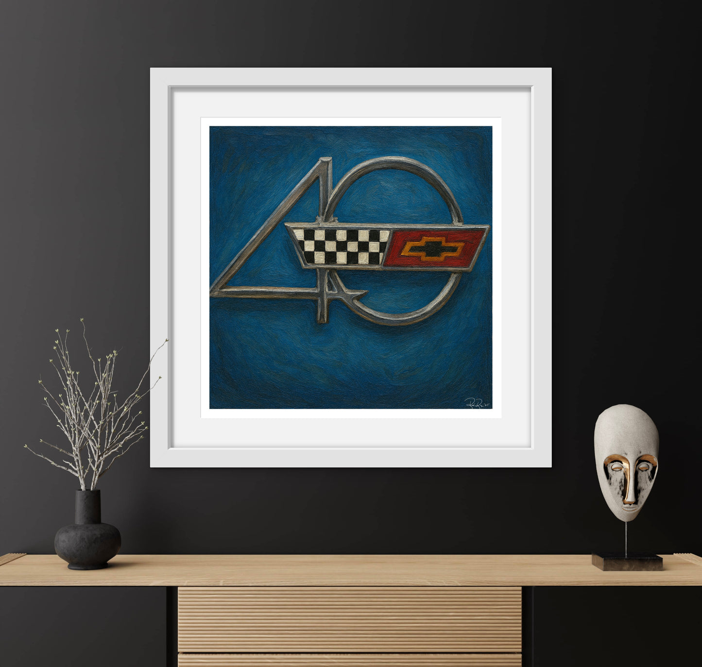 Framed artwork of a car emblem on a blue background, displayed on a wooden shelf with decorative items.