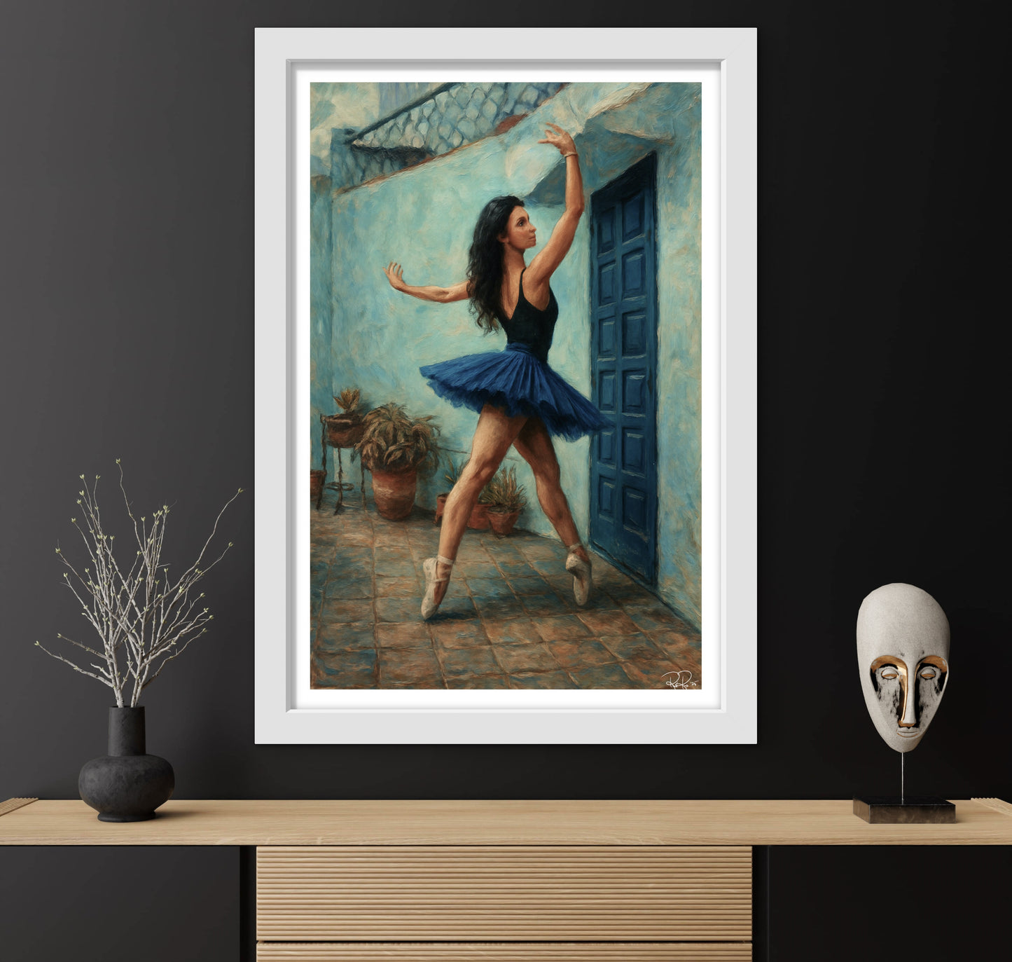 Framed artwork of a ballerina in a blue tutu against a black wall with decorative items on a wooden surface.