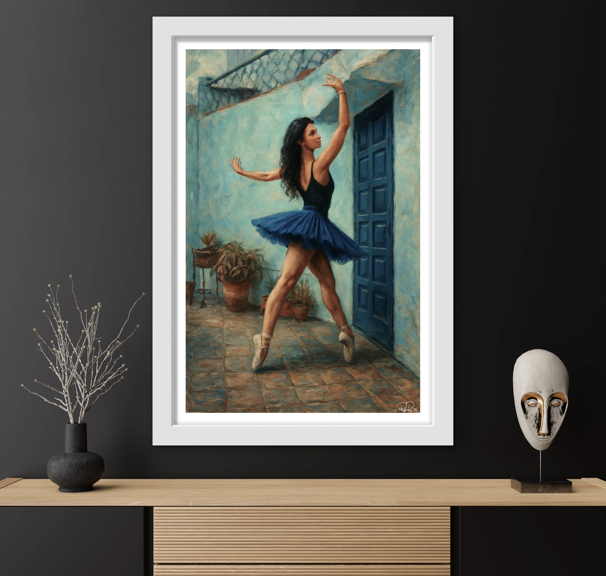 Framed artwork of a ballerina in a blue tutu against a black wall with decorative items on a wooden surface.