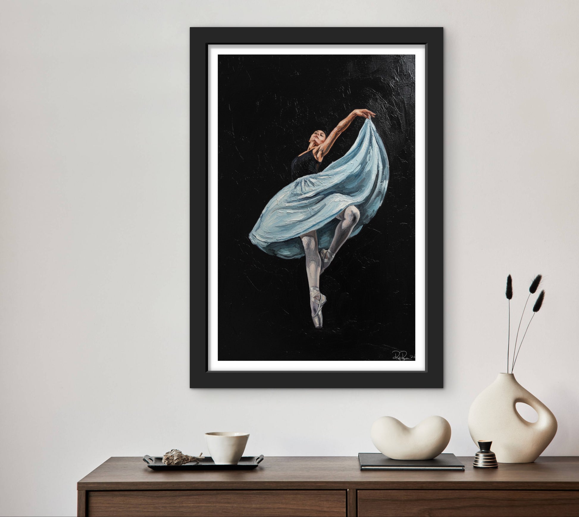 Framed artwork of a dancer with a blue skirt on a wall above a wooden console table.