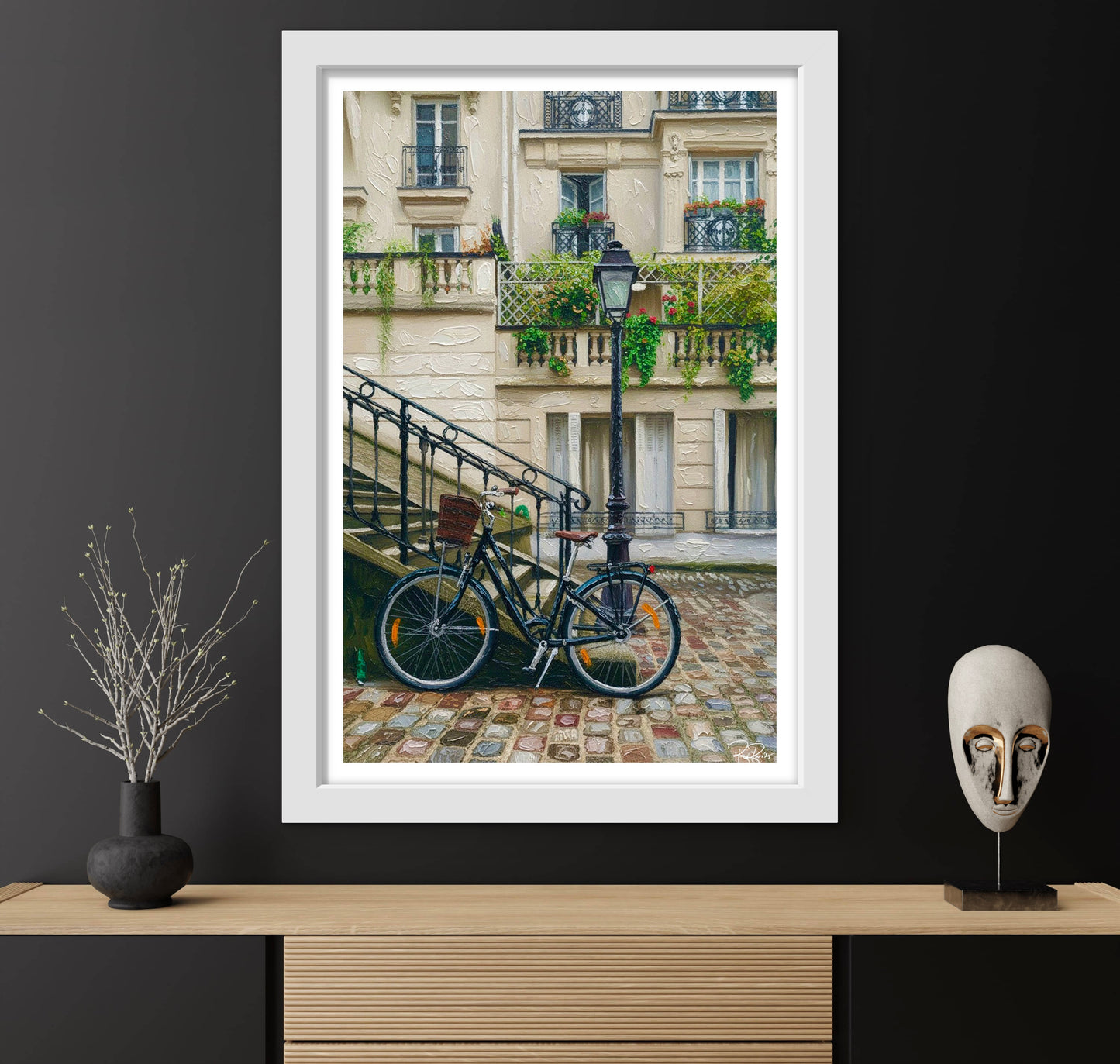 Framed photograph of a bicycle on a cobblestone street with a building in the background, displayed on a wooden shelf.