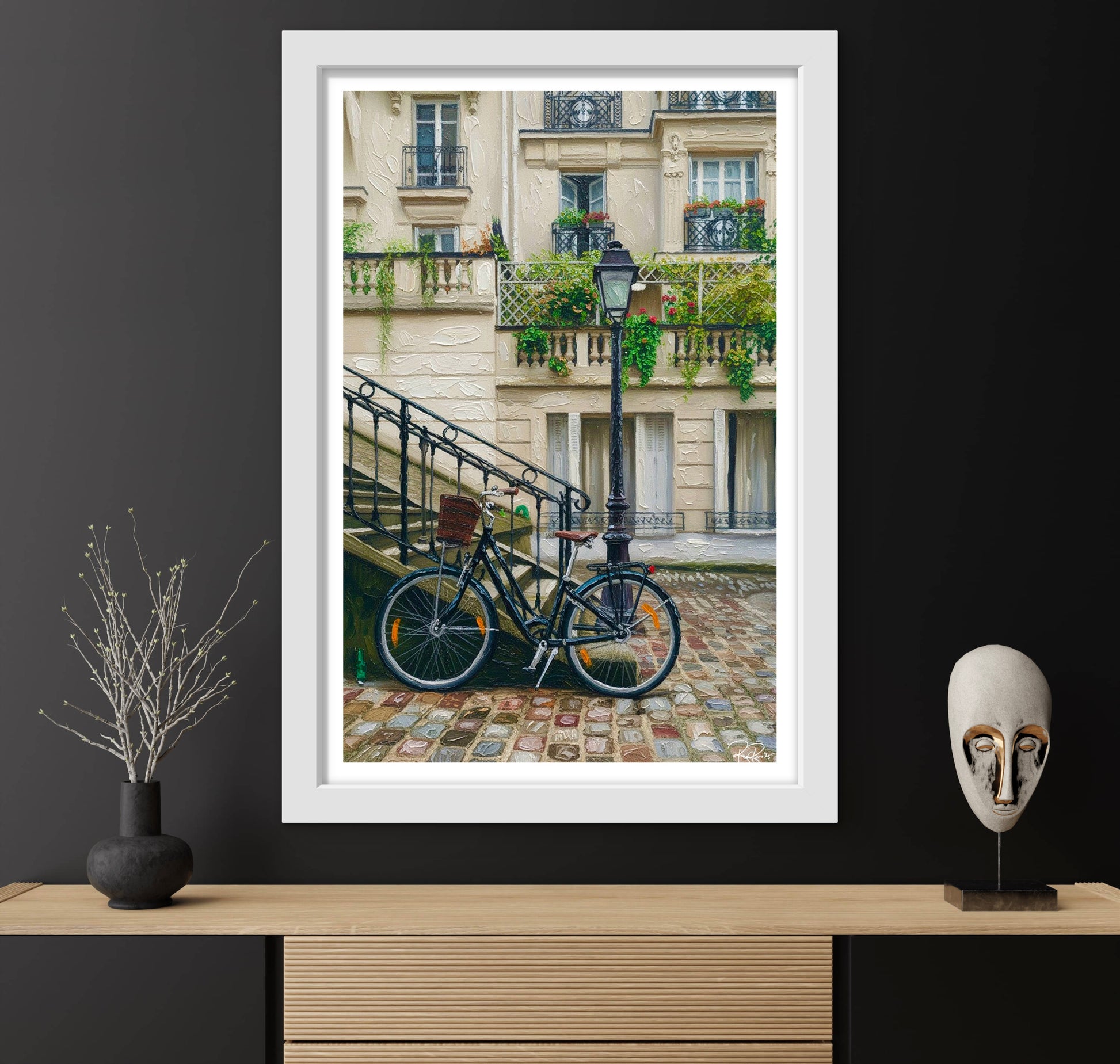 Framed photograph of a bicycle on a cobblestone street with a building in the background, displayed on a wooden shelf.