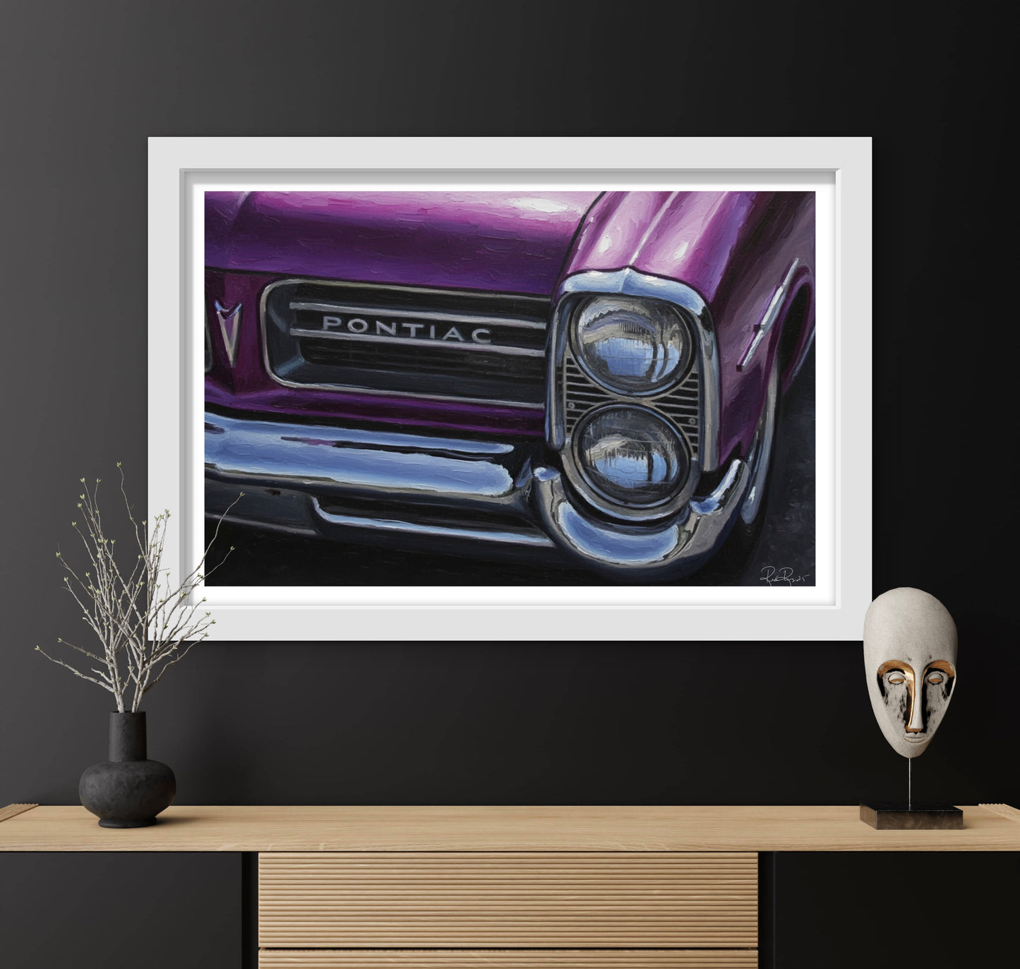 Framed artwork of a purple Pontiac car on a black wall with decorative items below.