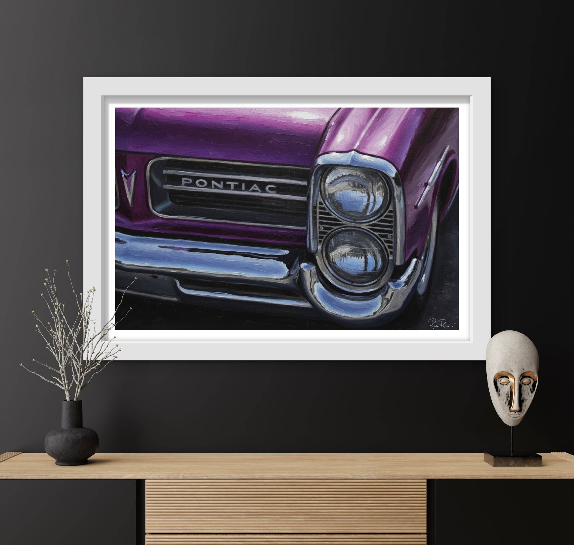 Framed artwork of a purple Pontiac car on a black wall with decorative items below.