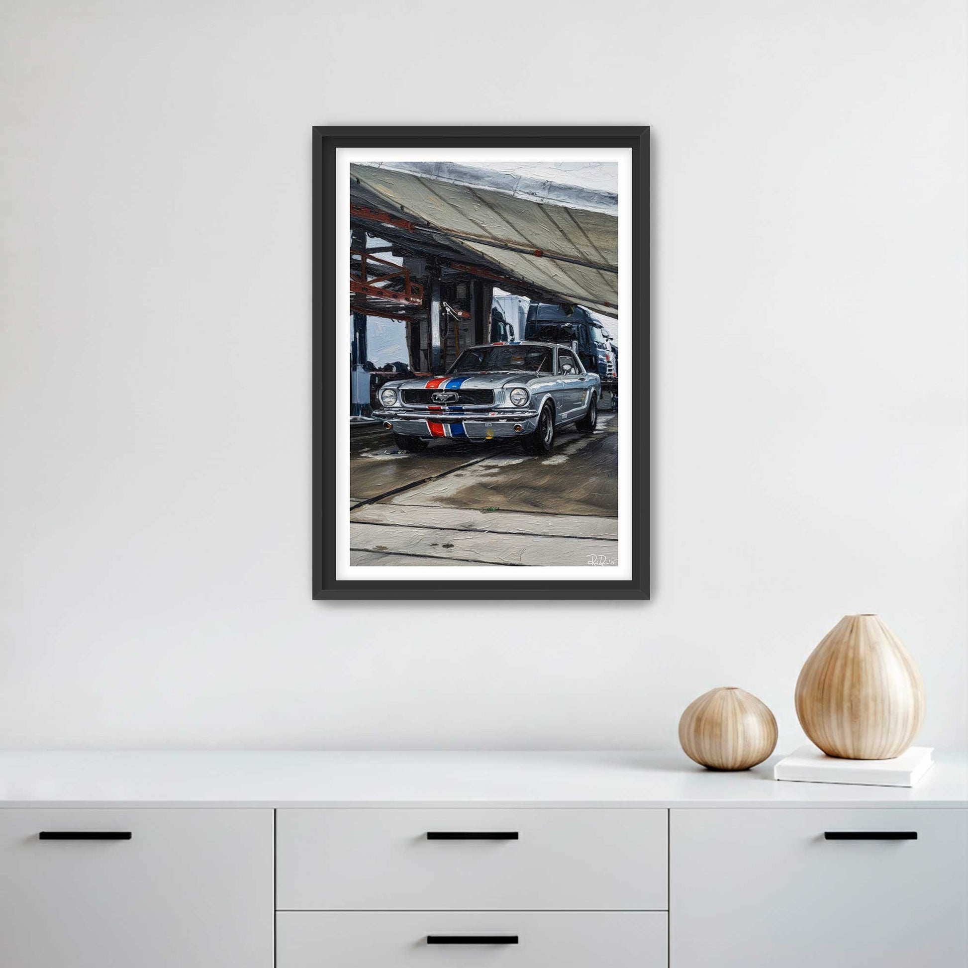 Framed artwork of a classic car on a white wall above a white cabinet.