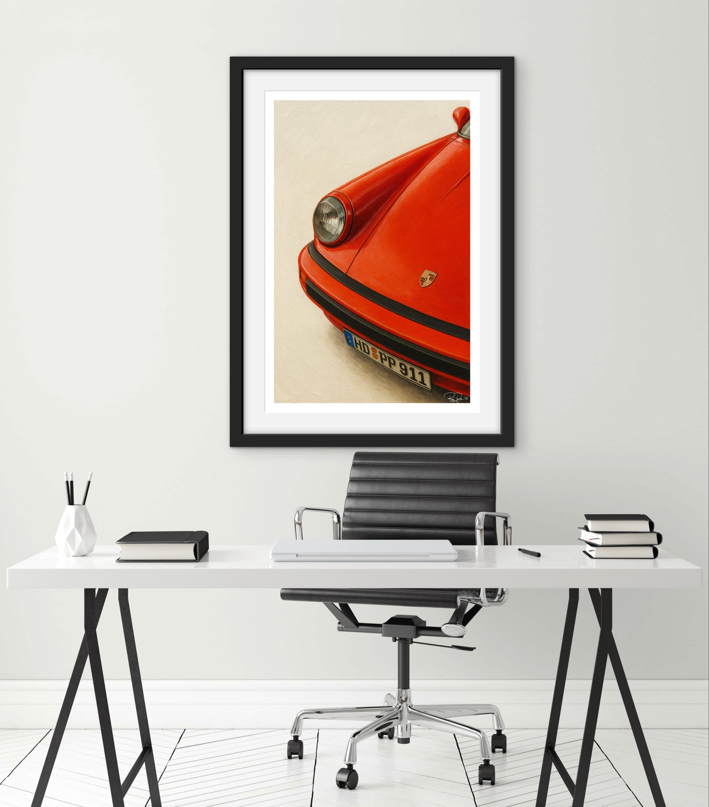 Framed artwork of a red car on a white wall above a desk.