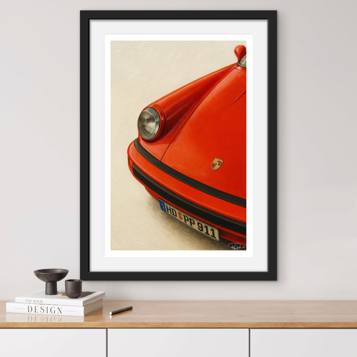 Framed poster of a red Porsche 911 on a wall above a wooden shelf.