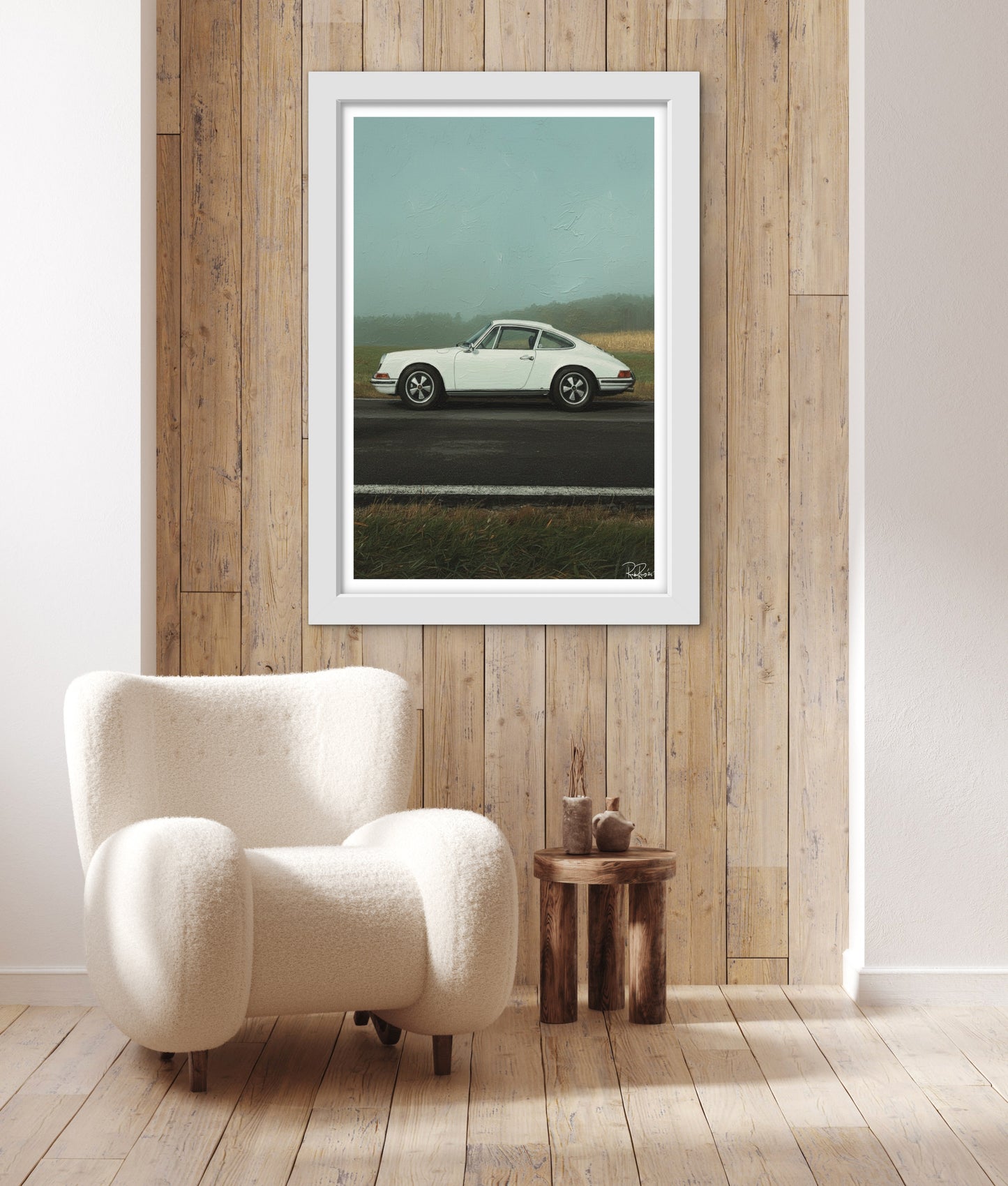 Framed artwork of a vintage car on a wooden wall above a white armchair.
