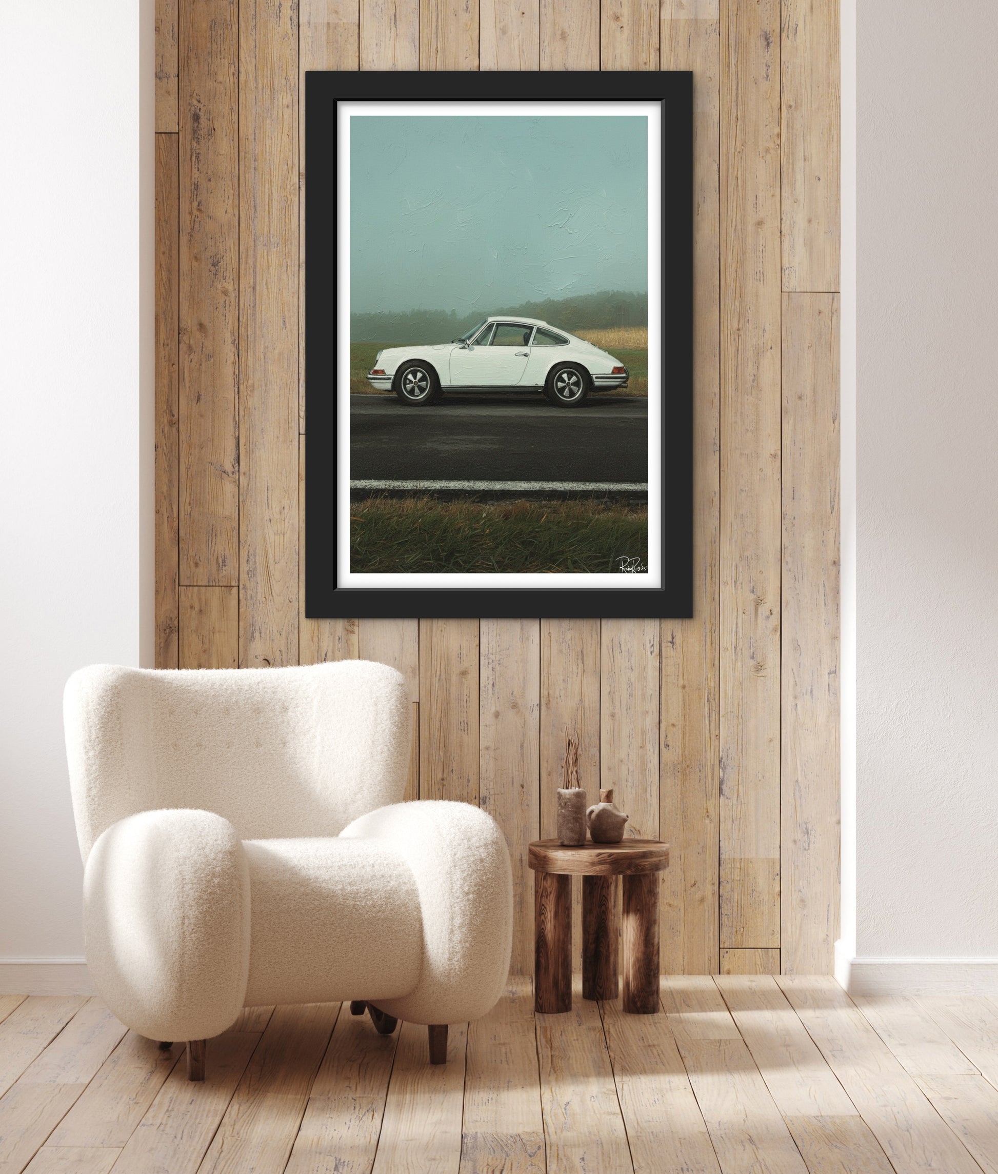 Framed artwork of a white car on a road in a room with wooden walls and a white armchair.