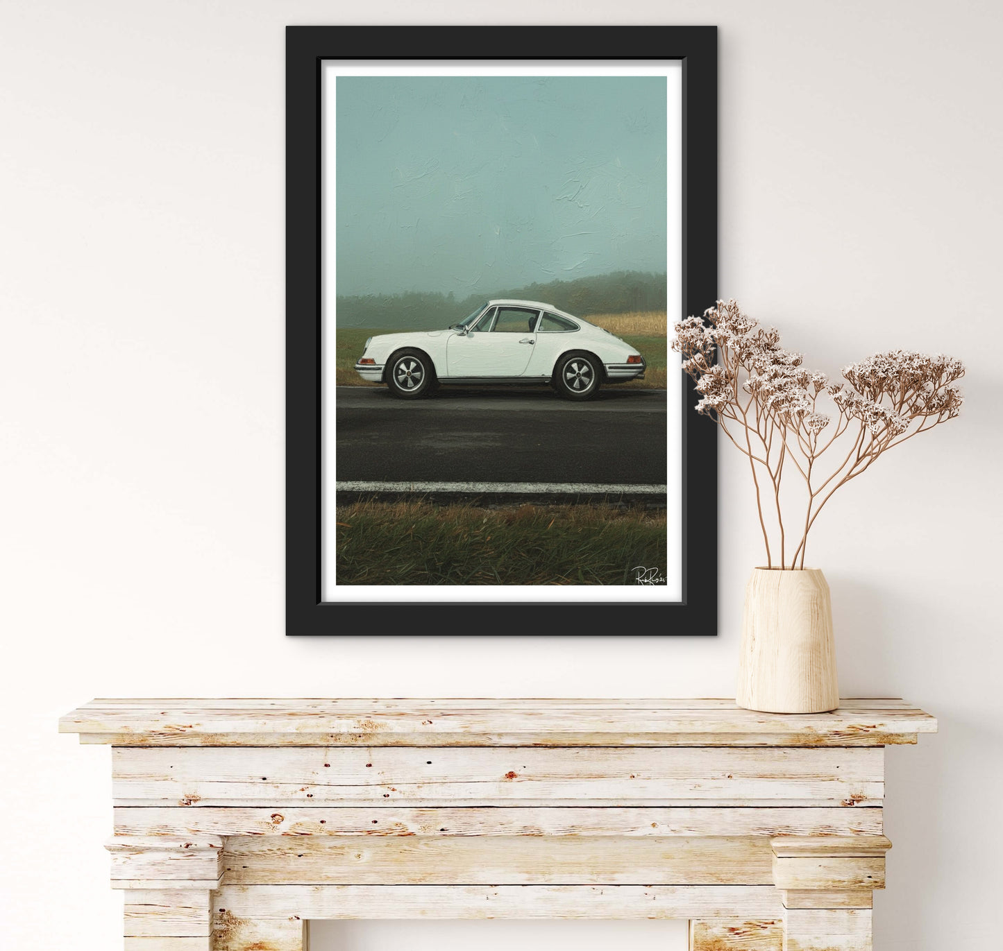 Framed artwork of a white car on a road with a vase of flowers on a wooden surface.