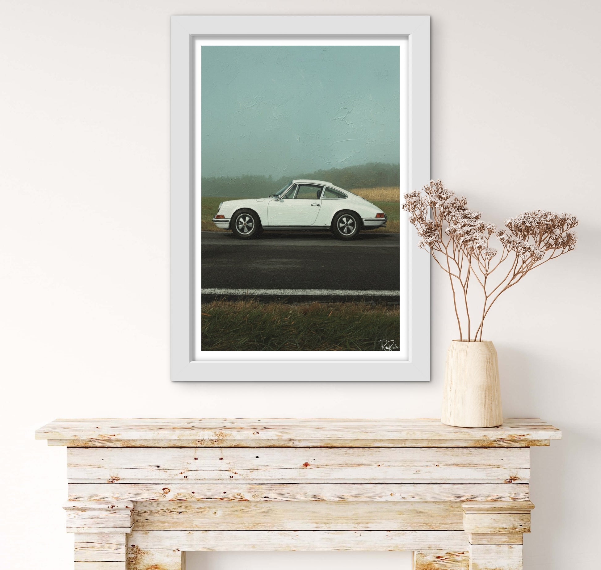 Framed artwork of a white car on a road with a vase of flowers on a wooden surface.