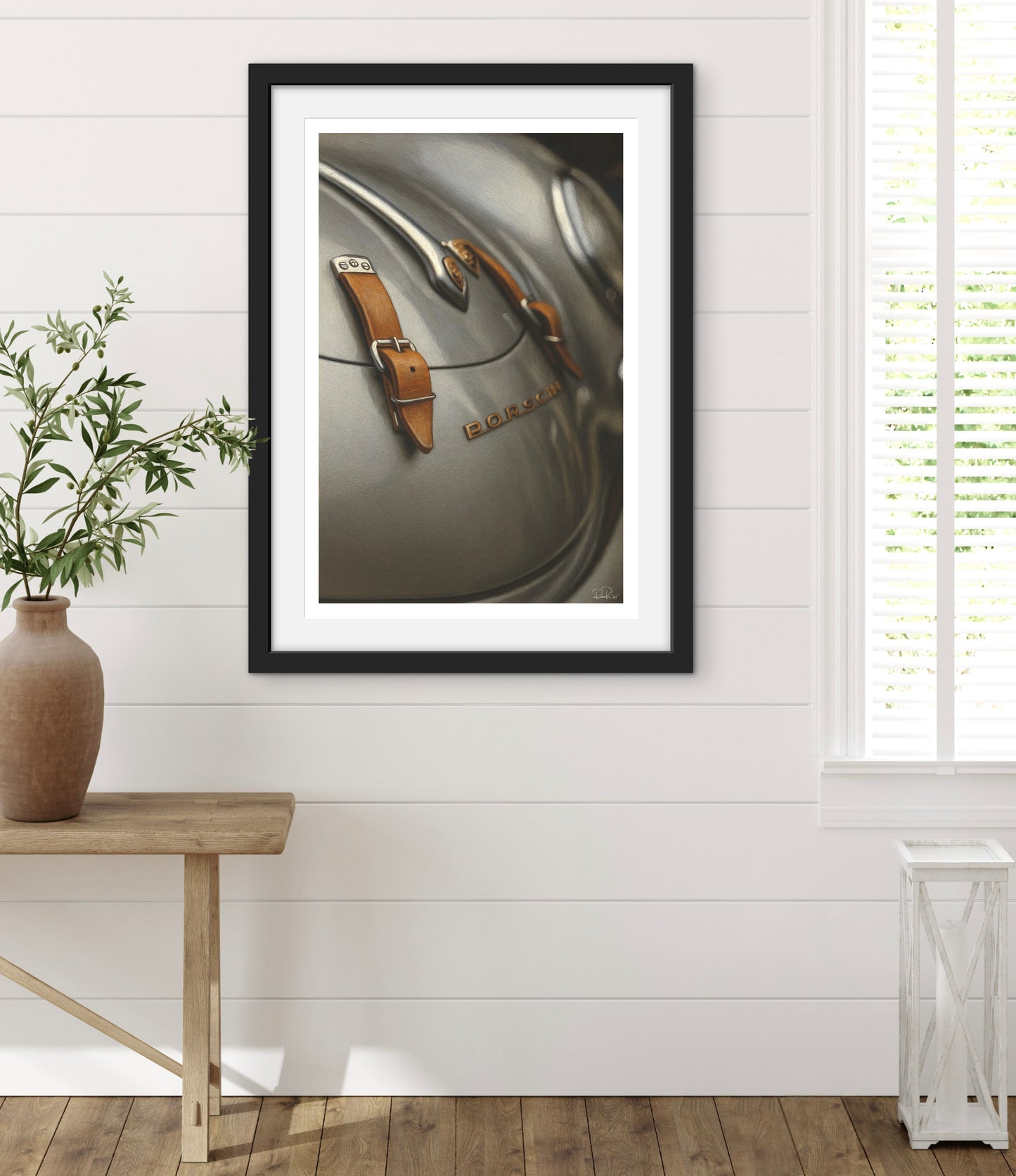Framed photograph of a vintage suitcase on a white wall with a wooden table and plant in the foreground.