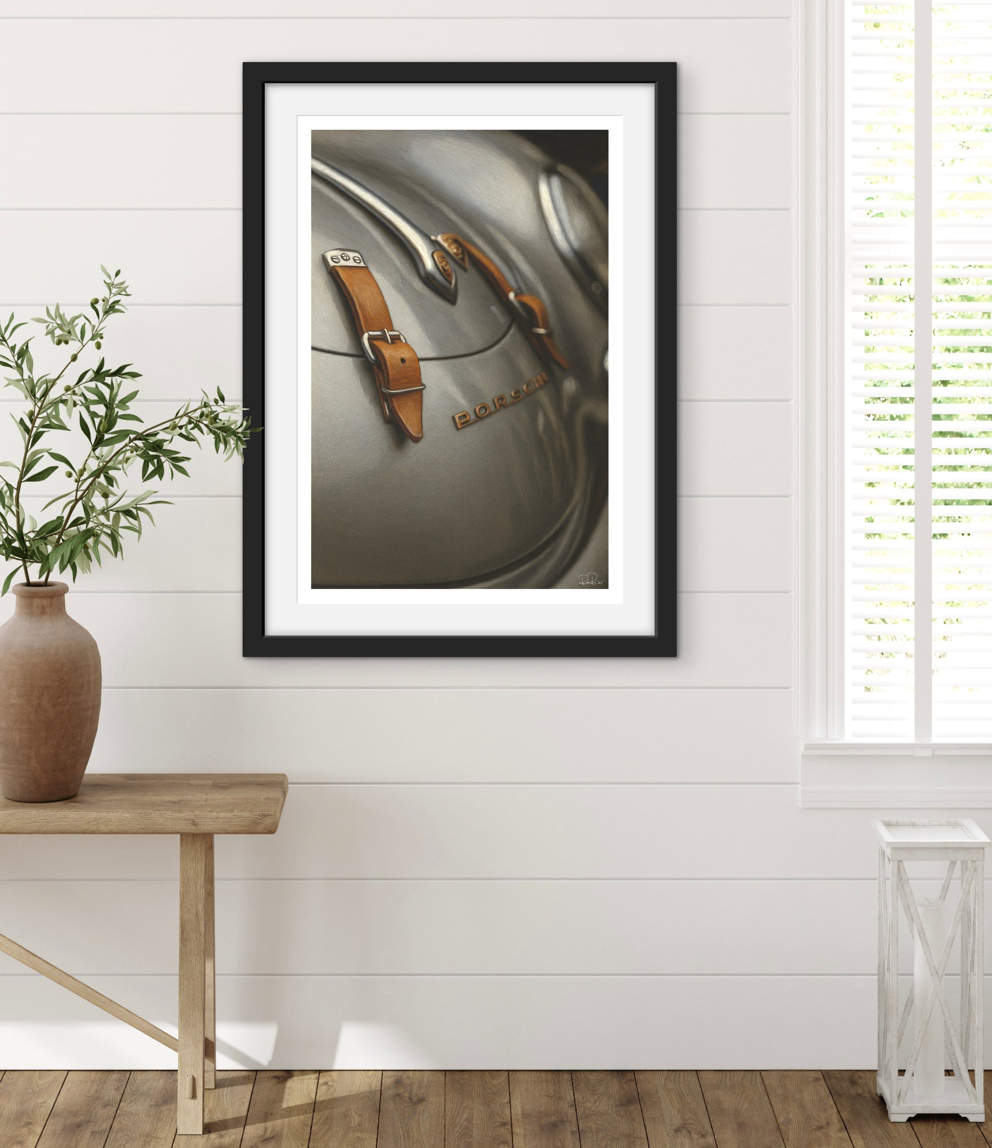 Framed photograph of a vintage suitcase on a white wall with a wooden table and plant in the foreground.