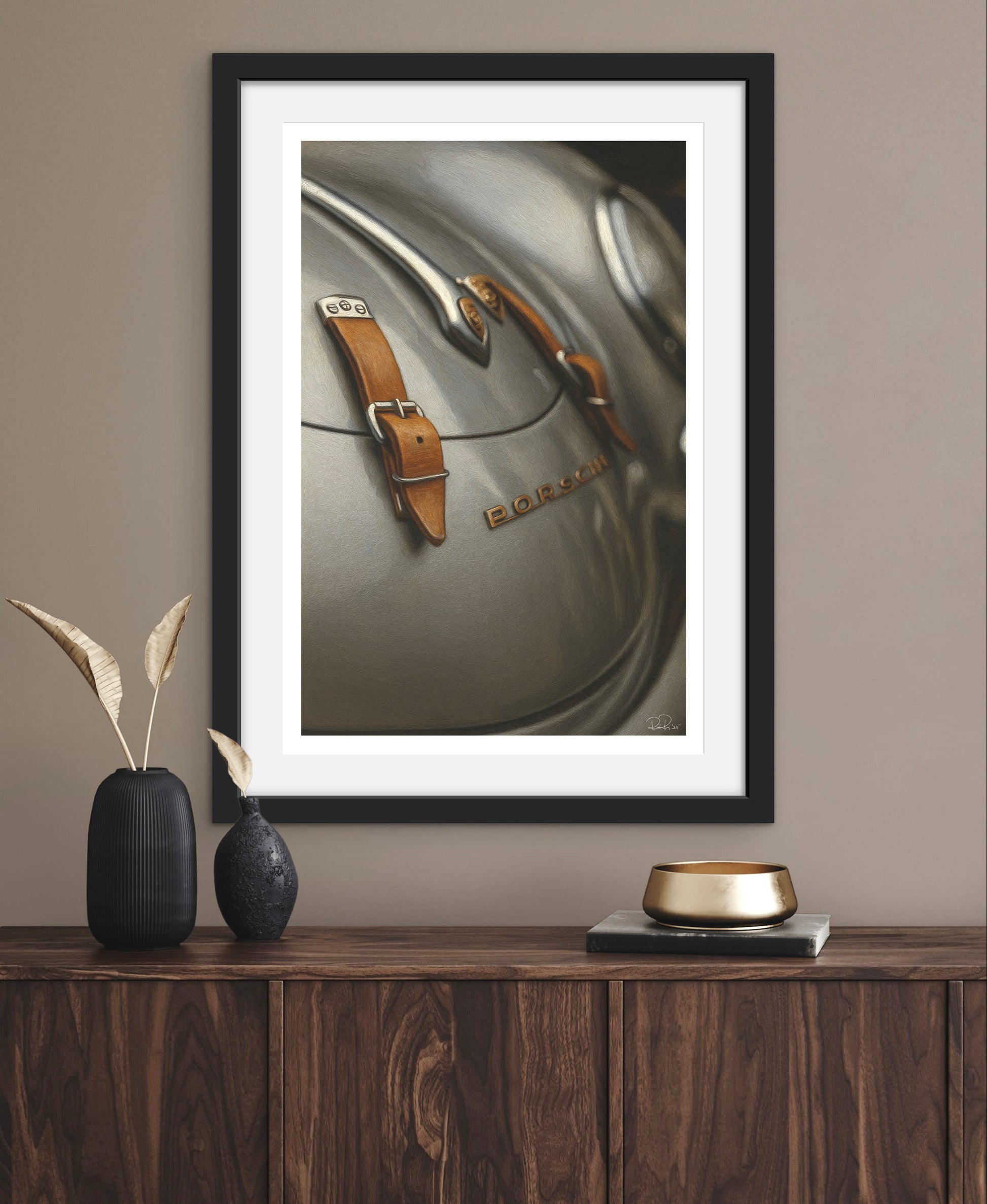 Framed artwork of a car emblem on a wall above a wooden cabinet with decorative items.