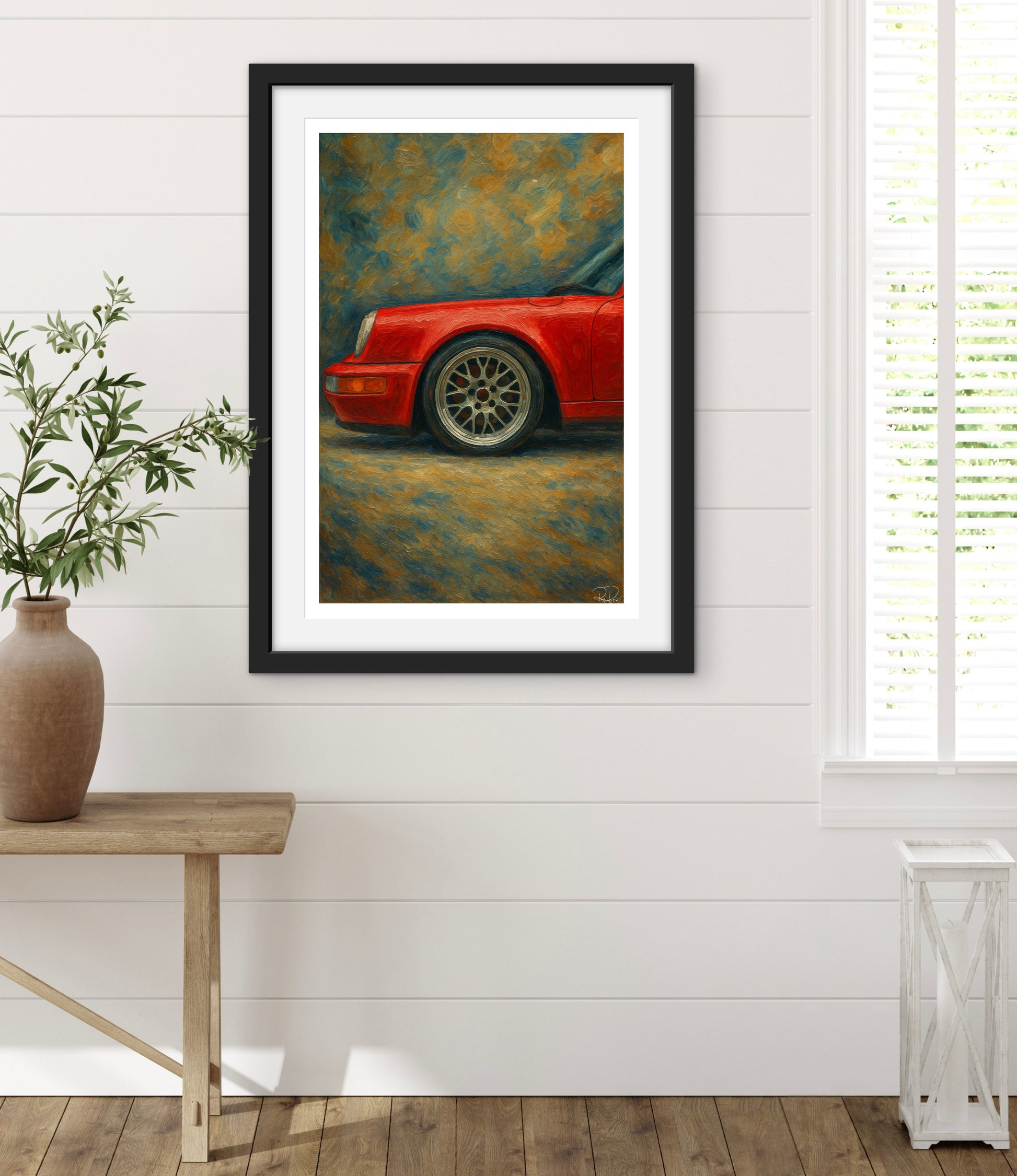 Framed artwork of a red car on a white wall with a wooden table and plant in the foreground.