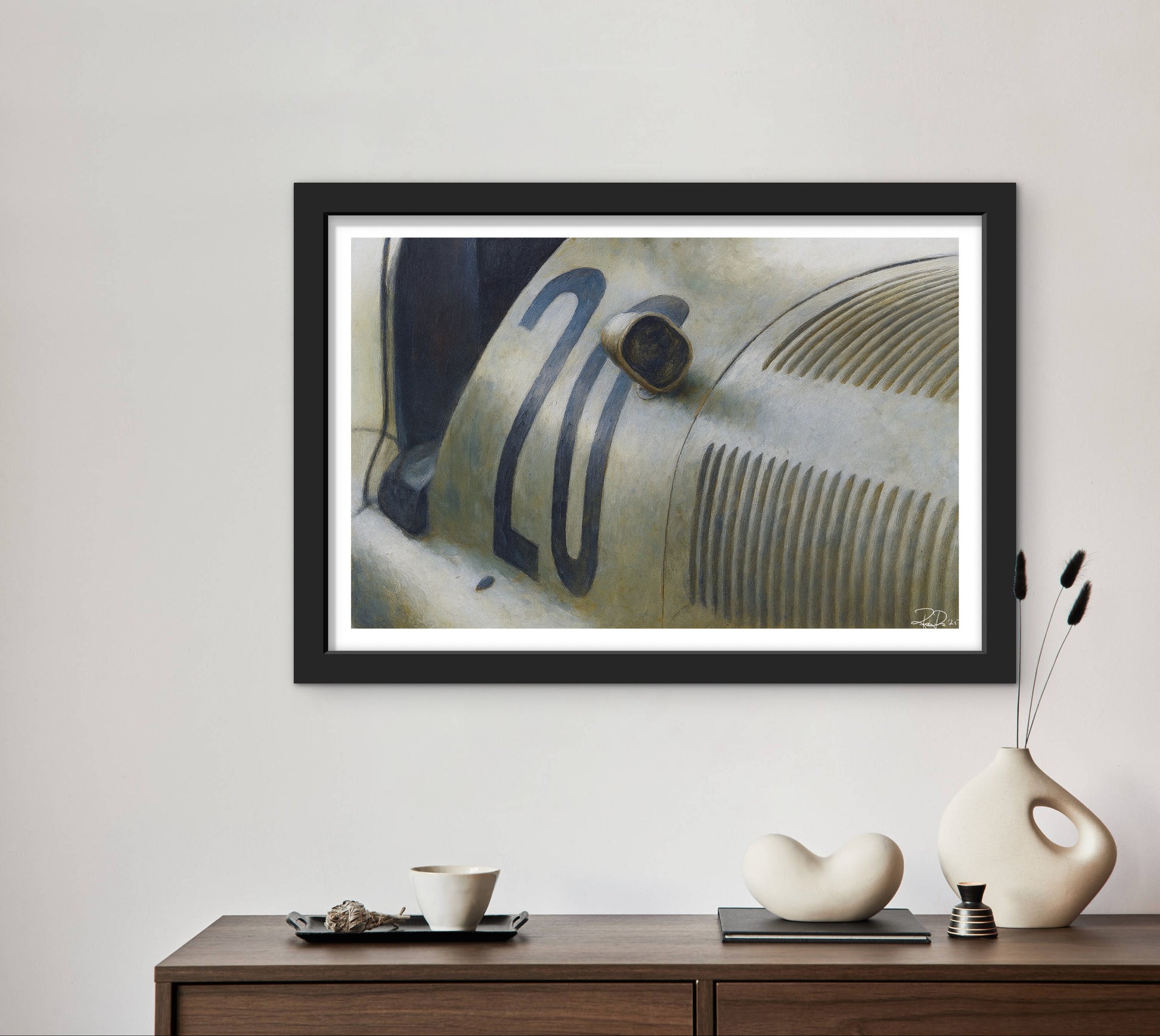 Framed artwork of a vintage car headlight on a wall above a wooden console table with decorative items.