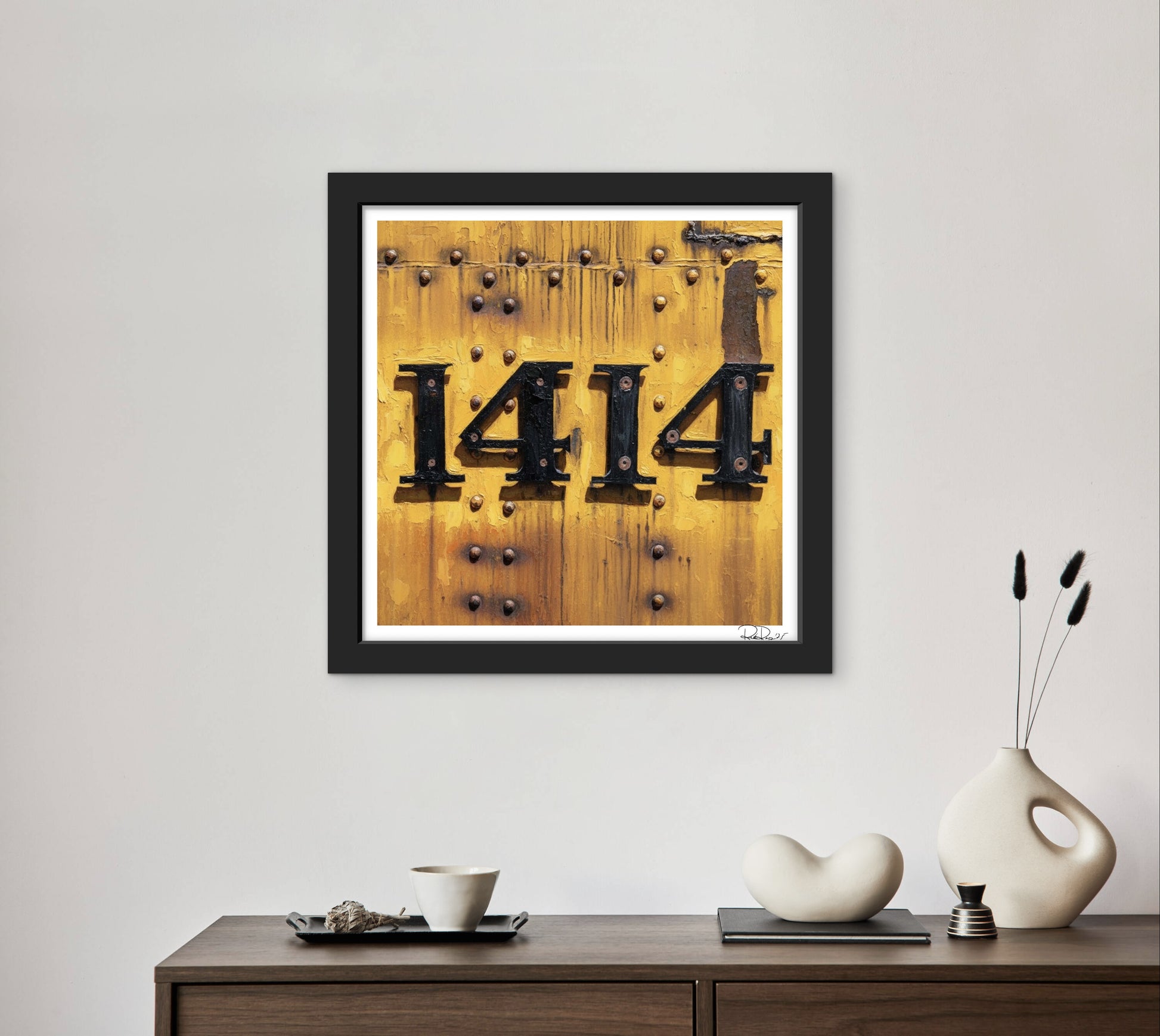 Framed artwork with '1414' on a wooden background above a console table with decorative items.