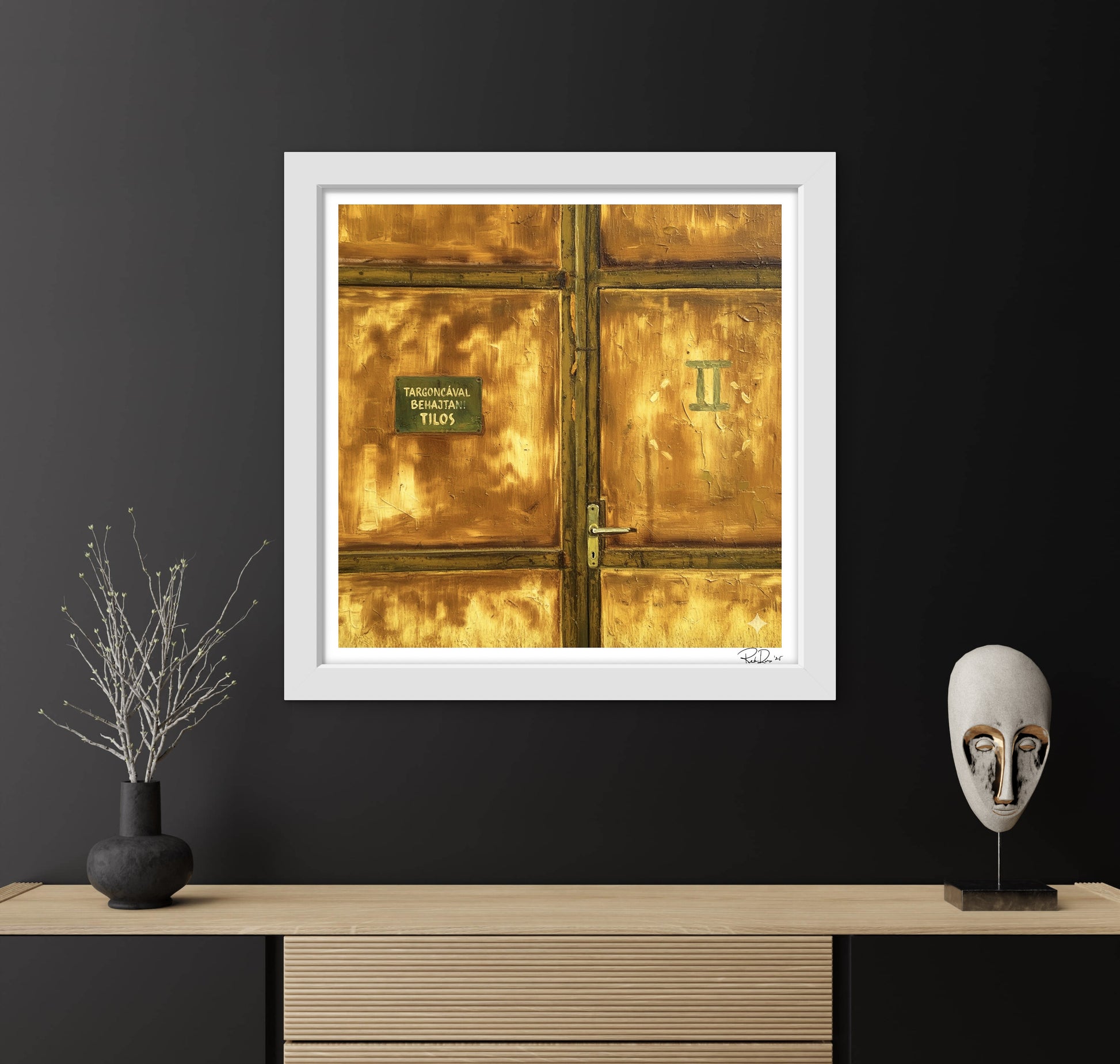 Framed artwork of a gold door on a black wall with decorative items below.