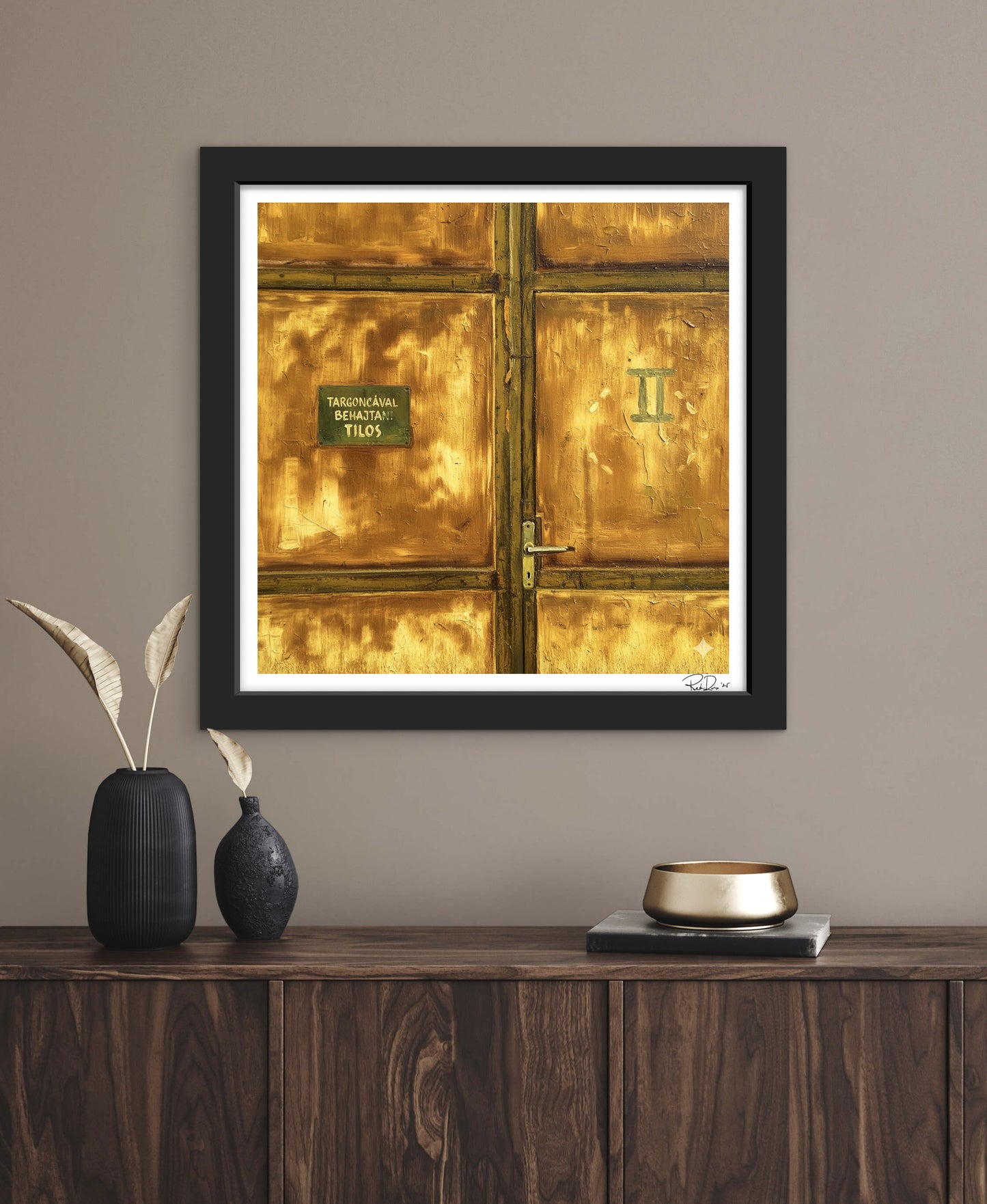 Framed artwork of a gold door with a black frame on a wall above a wooden console table.