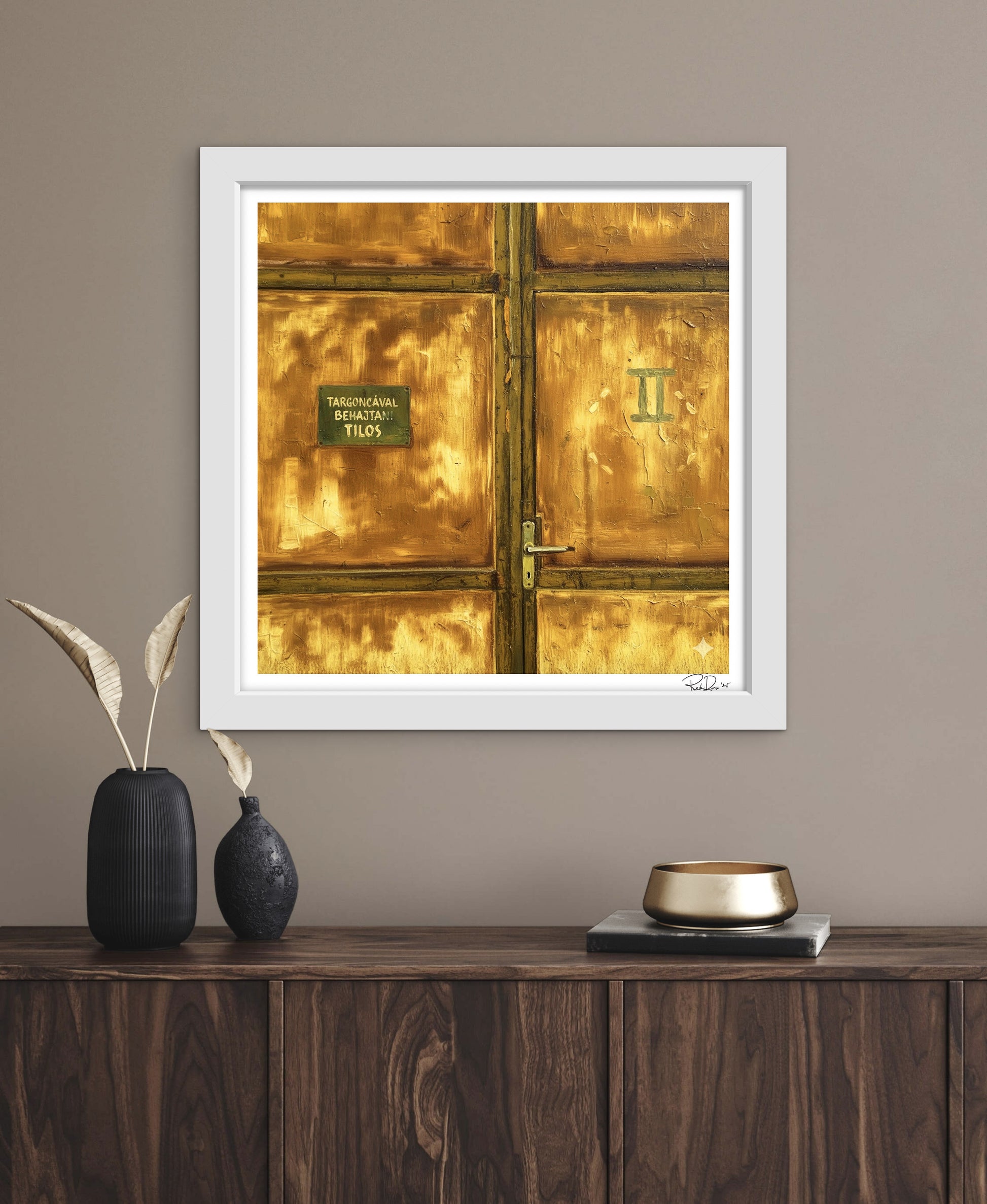Framed artwork of a gold door with a white frame on a wall above a wooden console table.