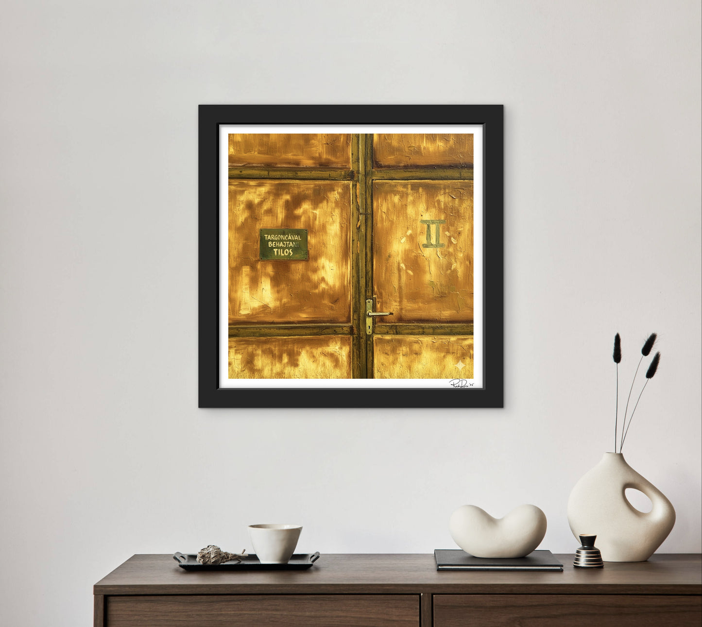 Framed artwork of a gold door on a wall above a wooden console table with decorative items.