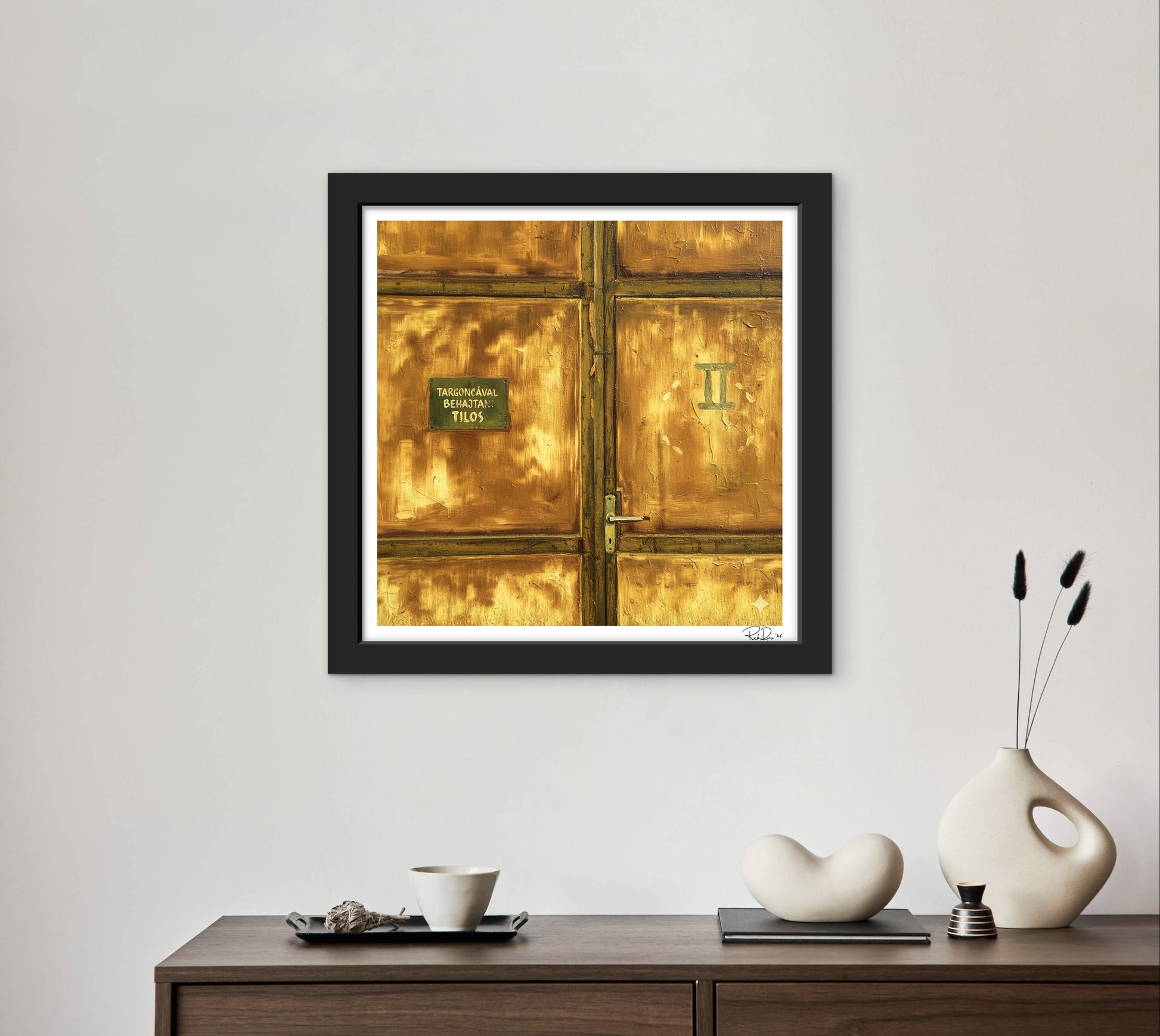Framed artwork of a gold door on a wall above a wooden console table with decorative items.