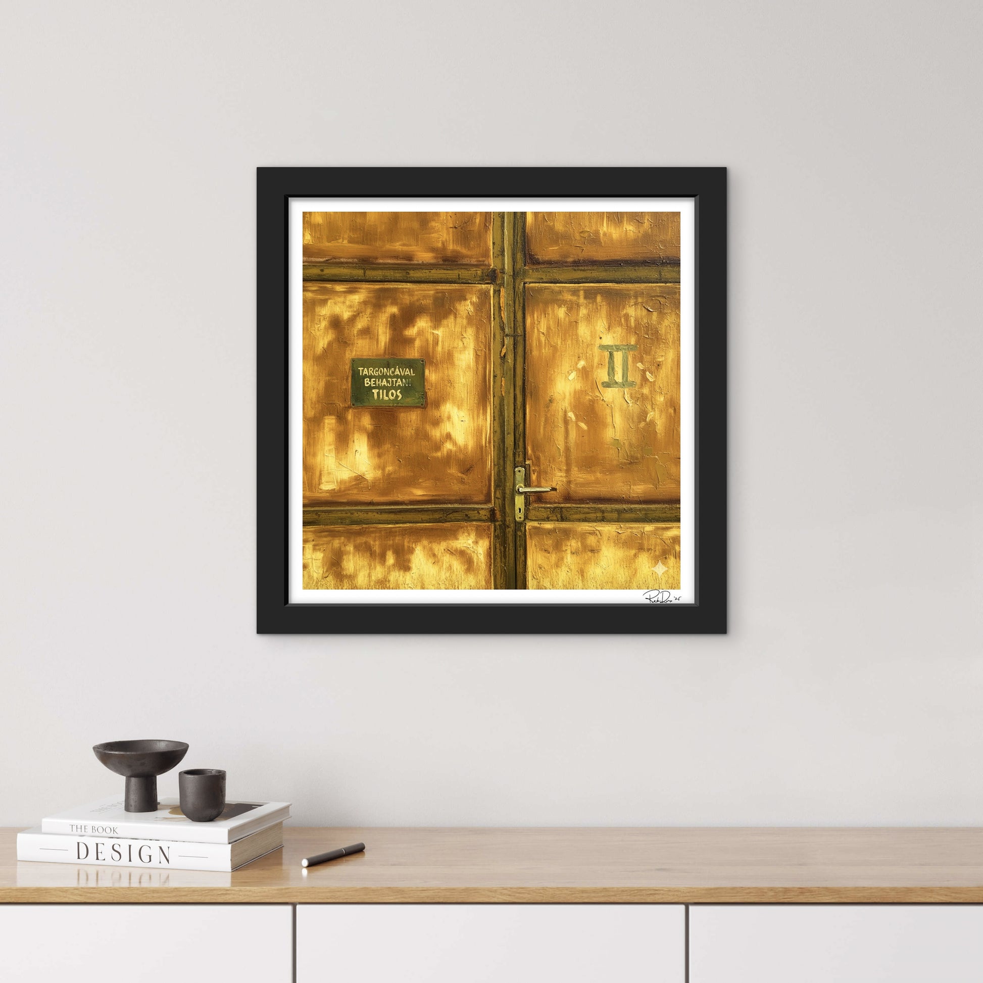 Framed photograph of a gold door on a white wall above a wooden desk.