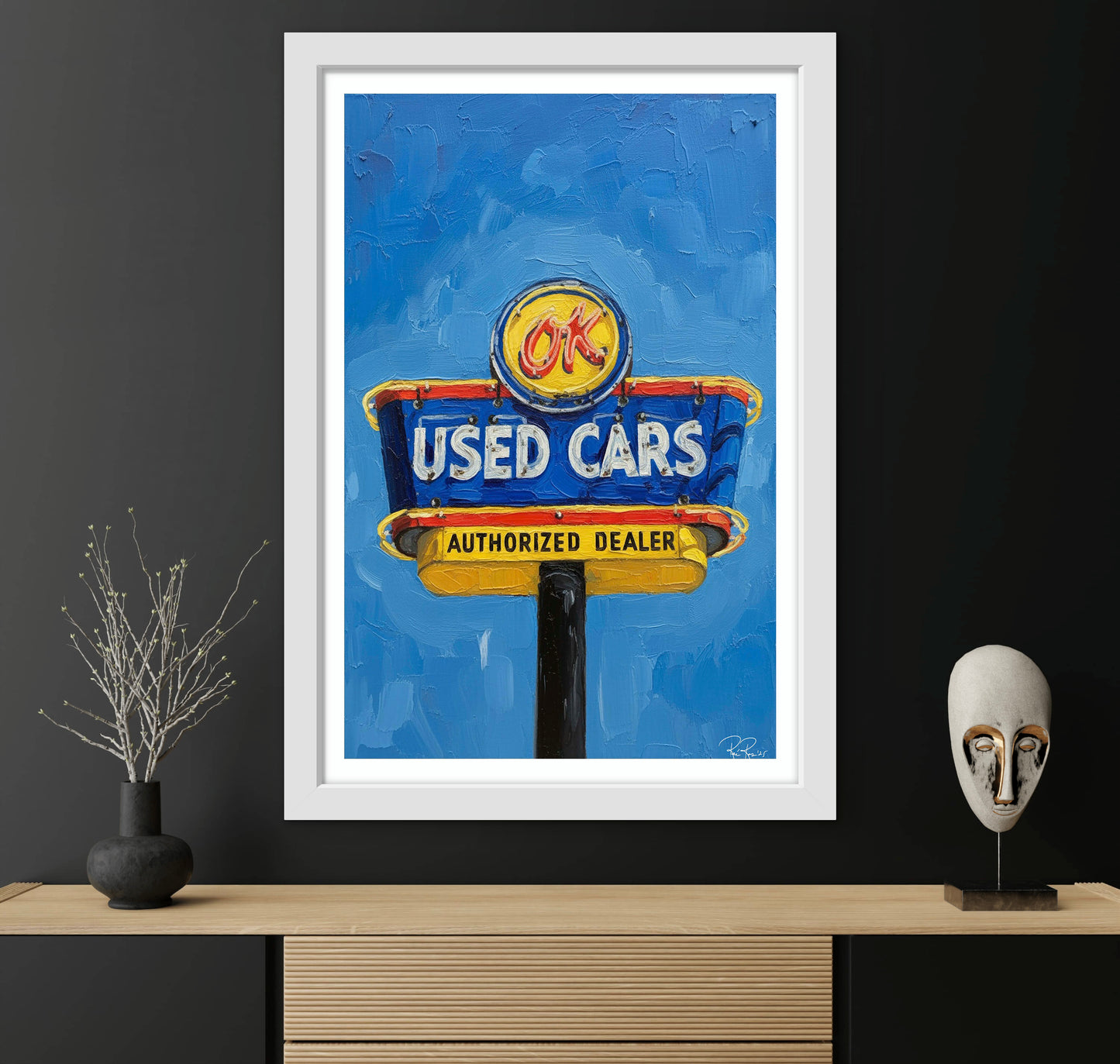 Framed artwork of a used cars sign on a black wall with decorative items.
