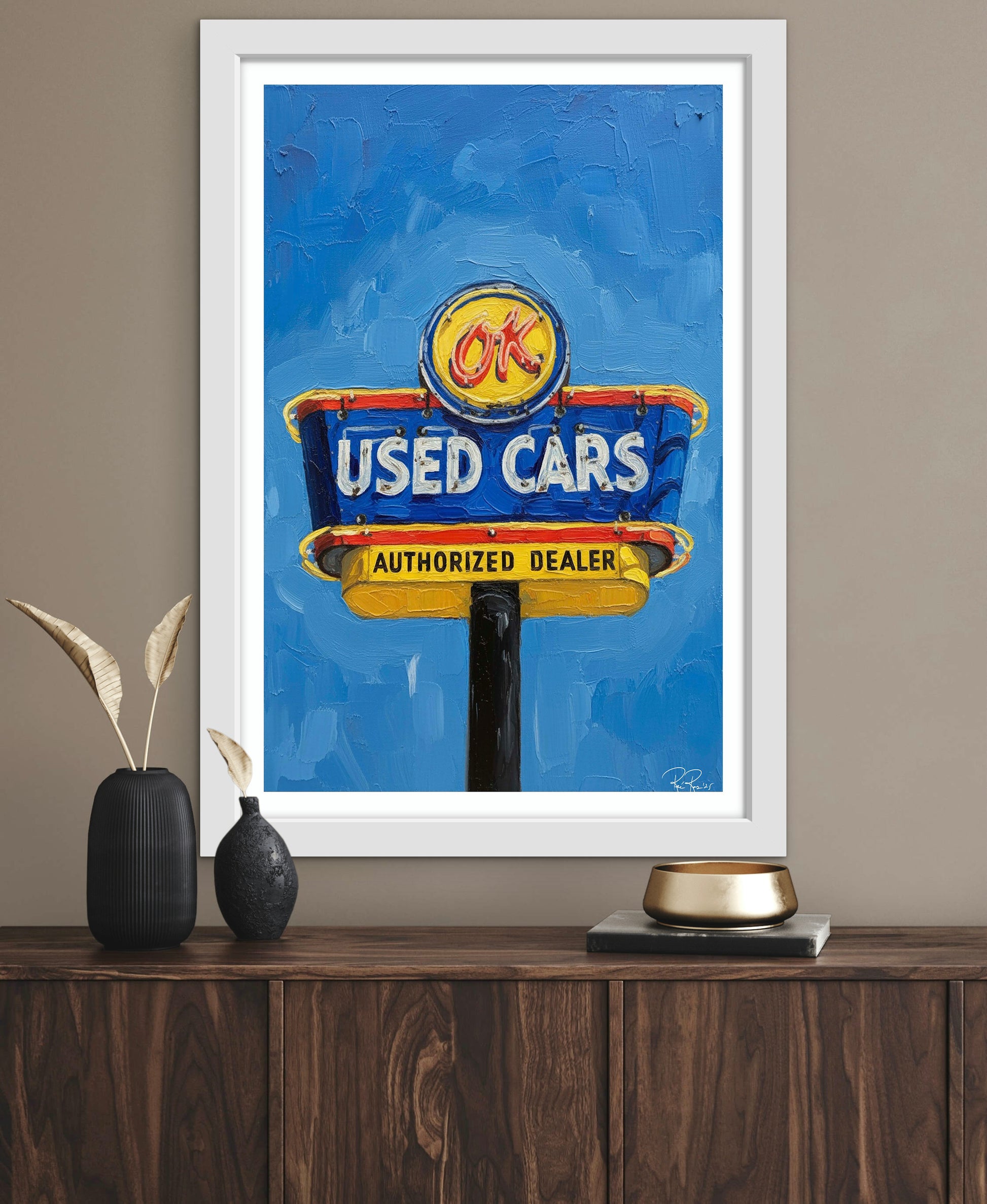 Framed artwork of a vintage 'OK Used Cars' sign on a wooden surface with decorative items.