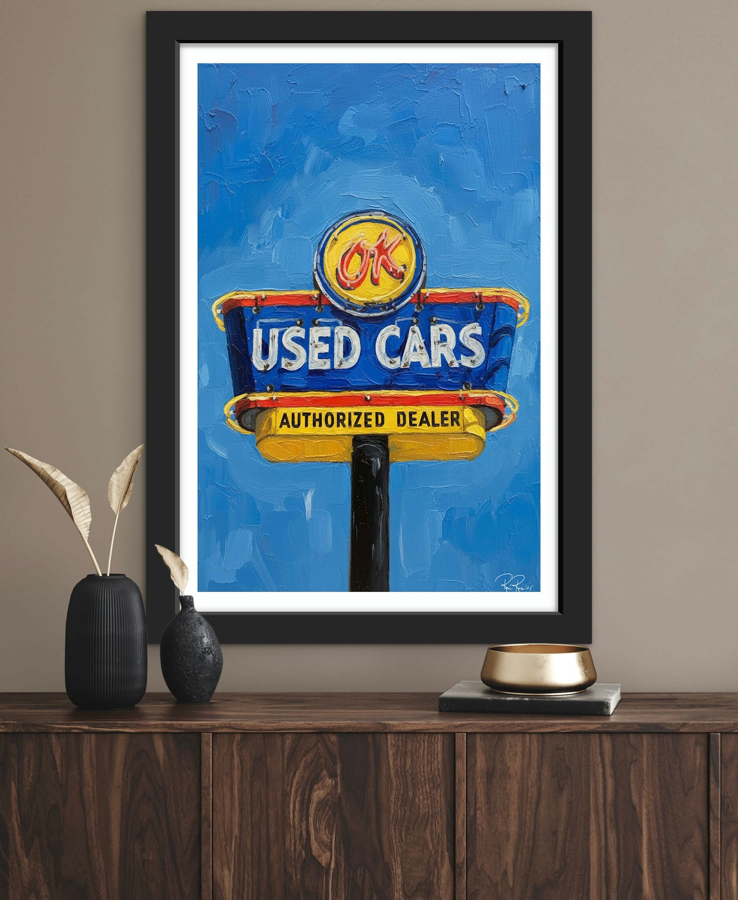 Framed artwork of a used cars sign on a wall above a wooden shelf.