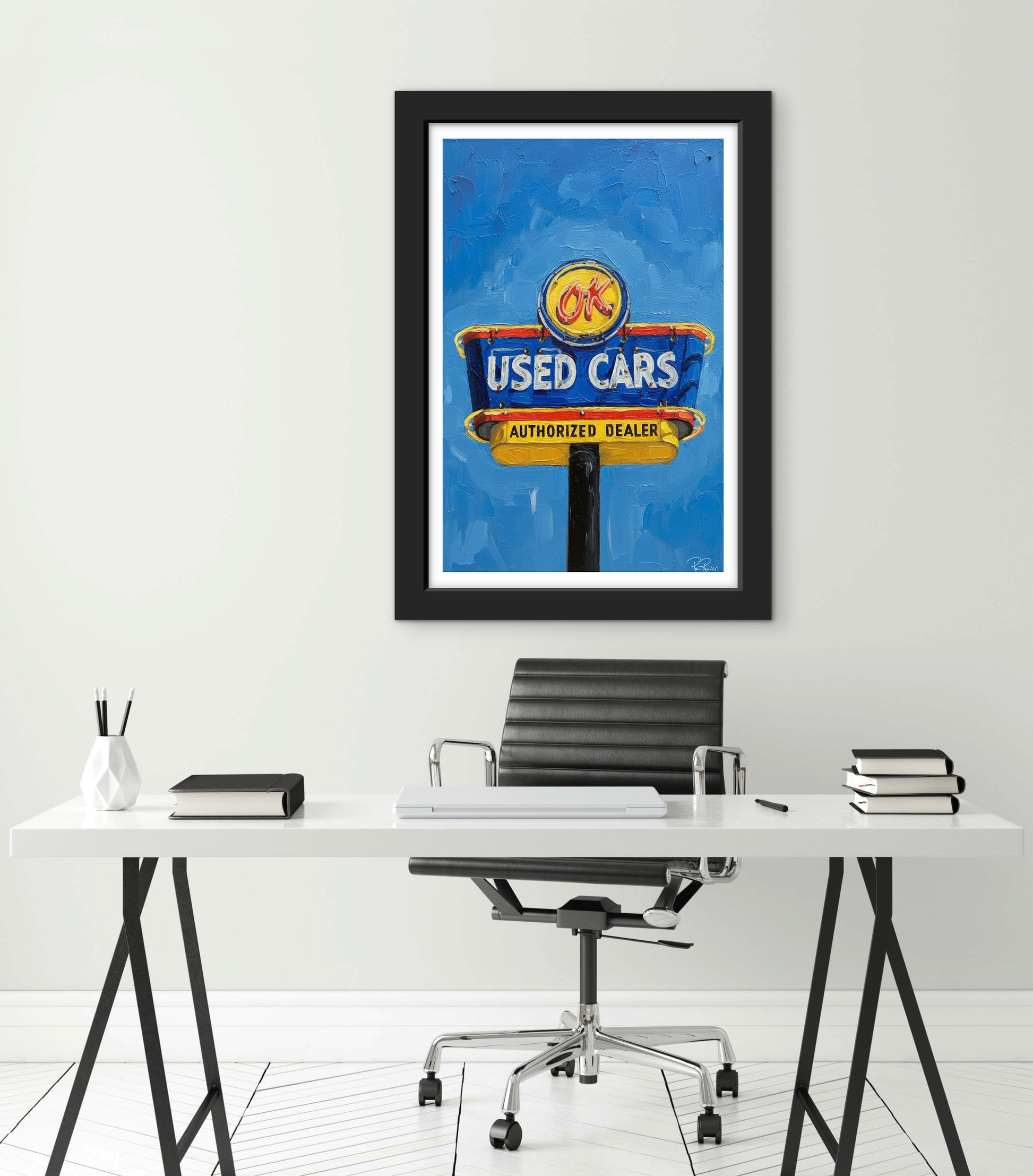 Framed poster of a used cars sign above a desk with office chair