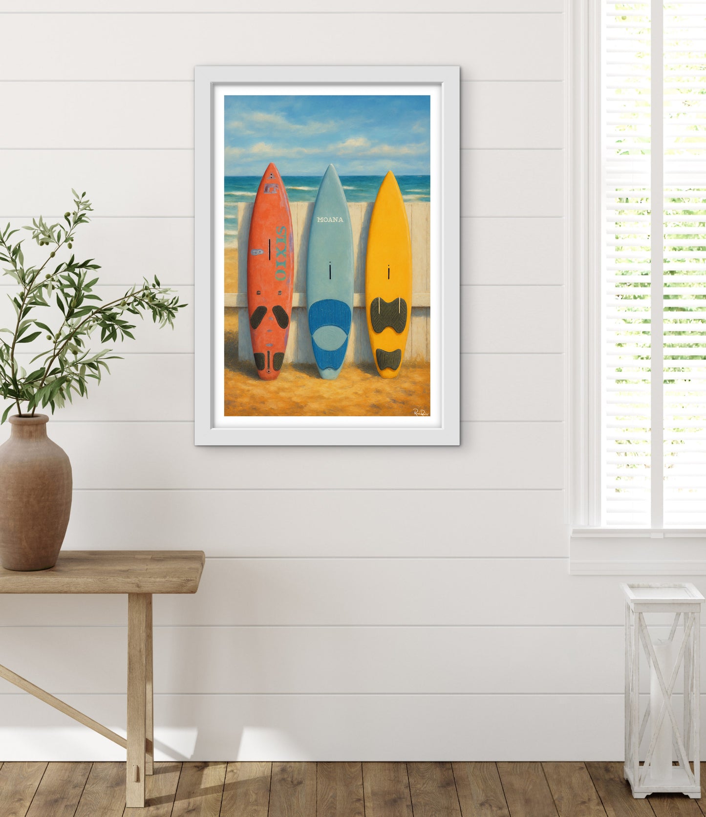 Framed artwork of surfboards on a beach wall in a room with a wooden table and plant.