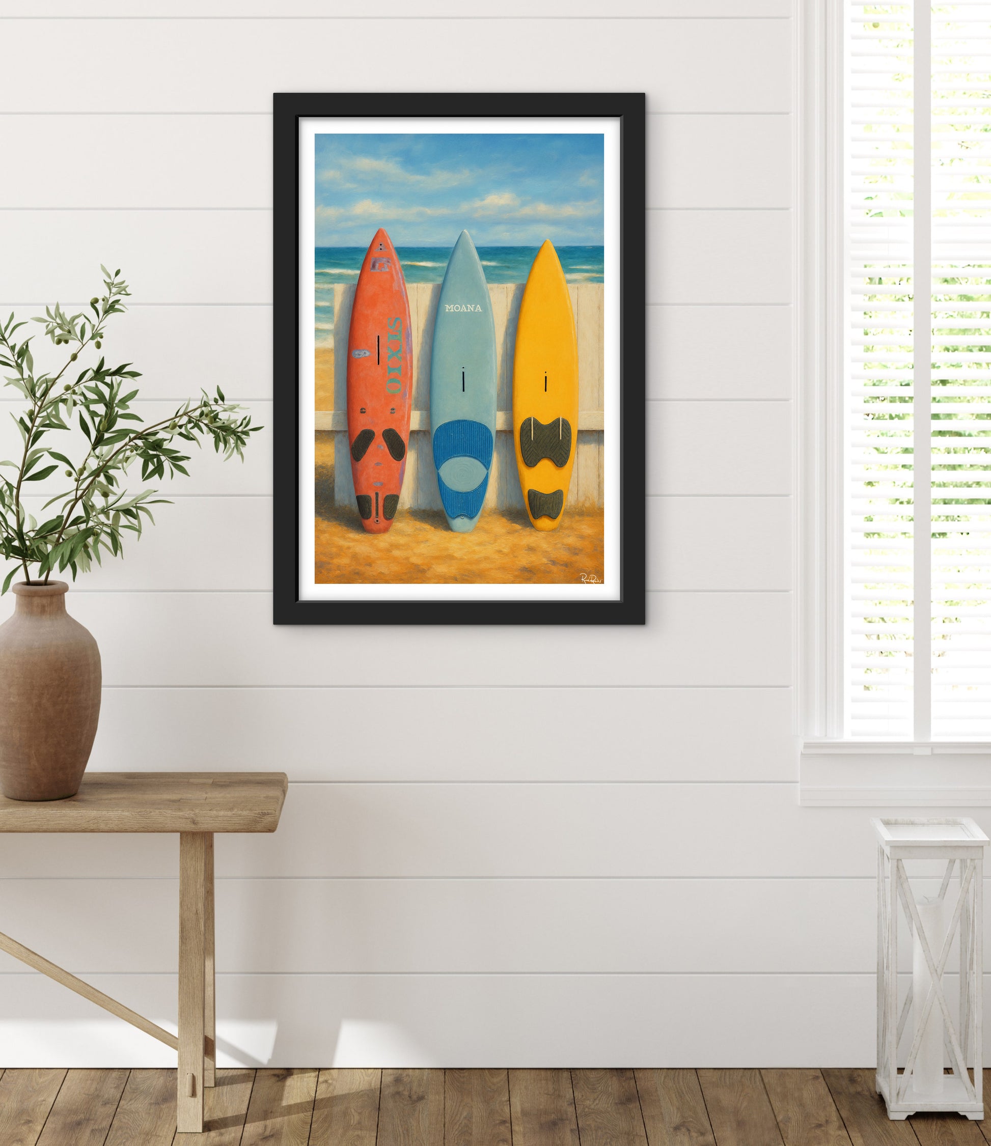 Framed artwork of surfboards on a beach wall in a room with a wooden floor and plant.