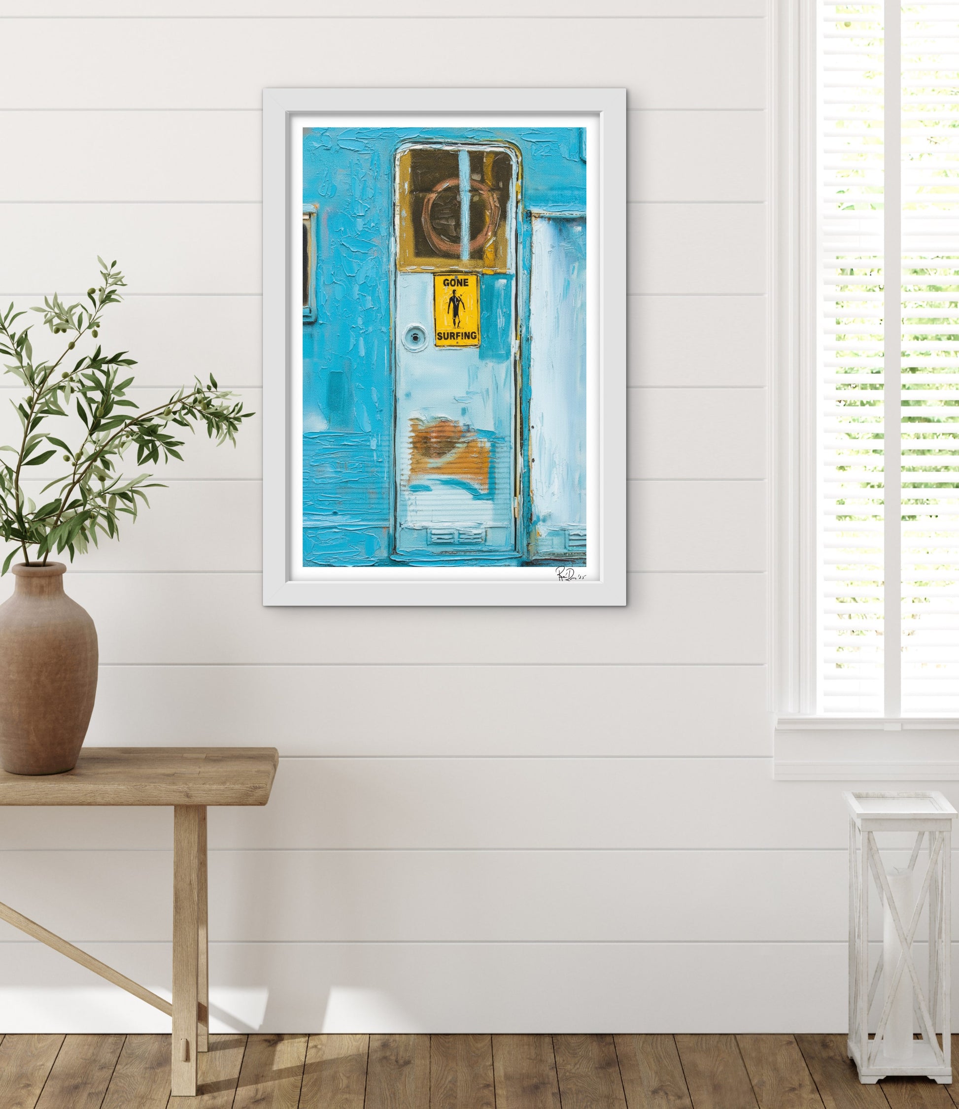 Framed artwork on a white wall with a wooden table and plant in the foreground.
