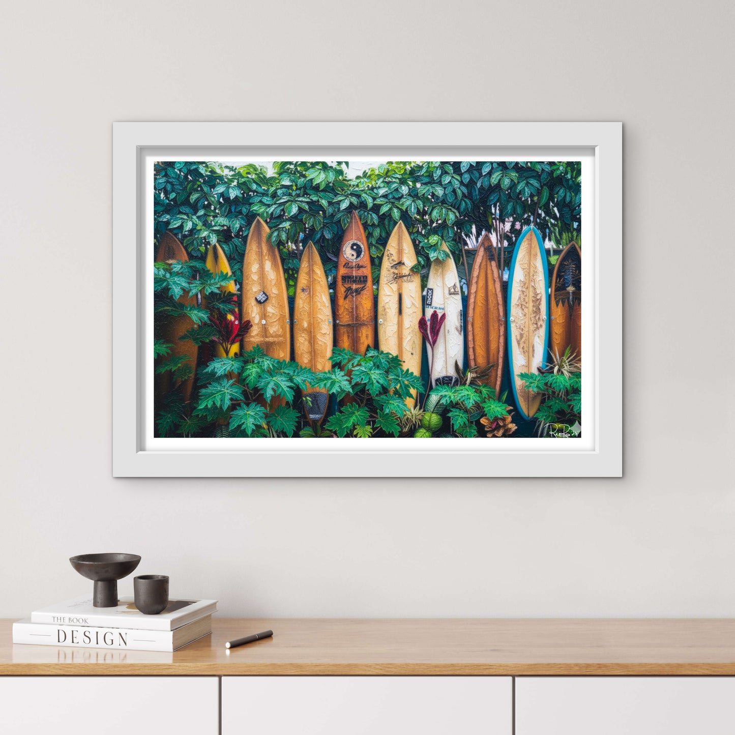 Framed artwork of surfboards in a forest displayed on a wall above a wooden shelf.