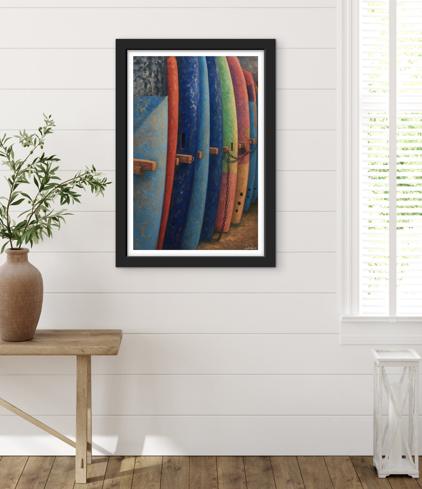 Framed artwork of colorful surfboards on a white wall with a wooden table and plant.