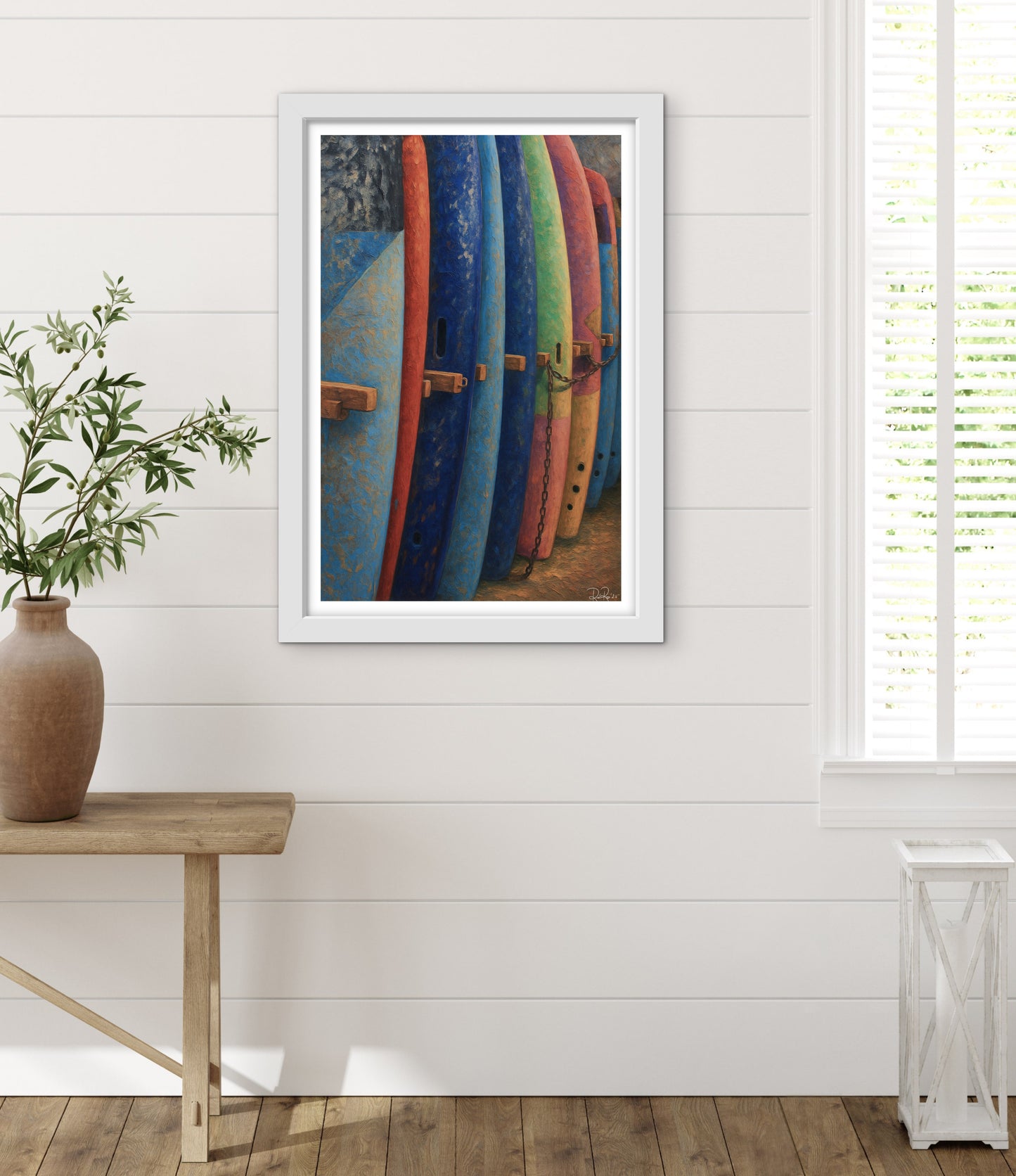 Framed artwork of surfboards on a white wall with a wooden table and plant in the foreground.