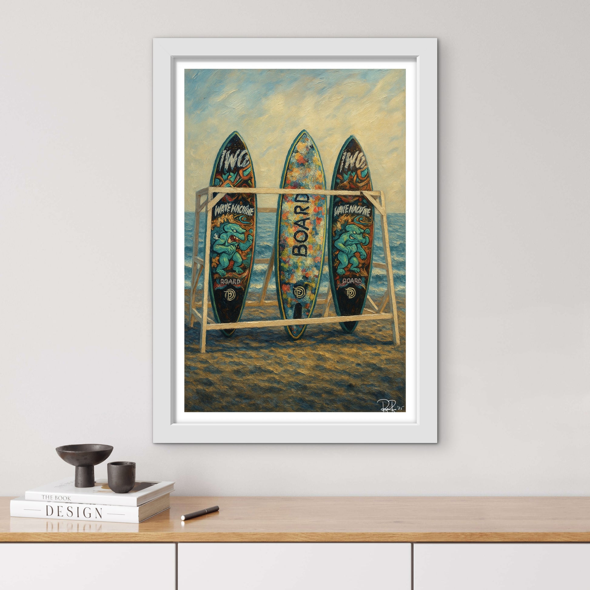 Framed artwork of surfboards on a beach with books and a pen on a wooden surface below.