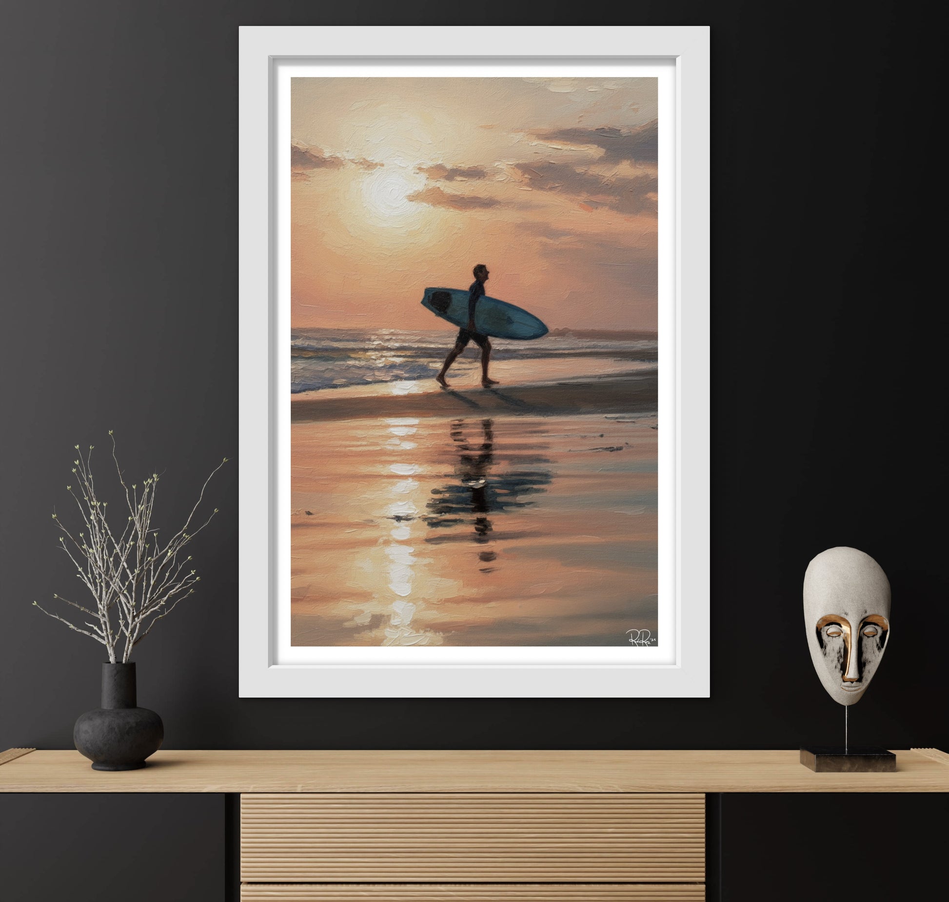 Framed photograph of a person with a surfboard walking on a beach at sunset, displayed on a wooden shelf.