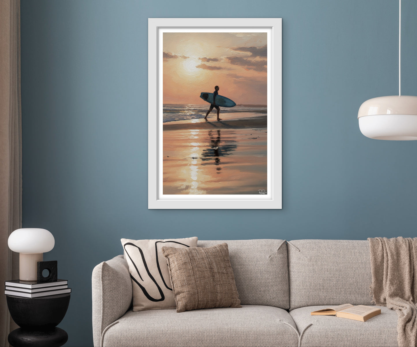 Framed artwork of a person with a surfboard at sunset on a wall above a sofa.
