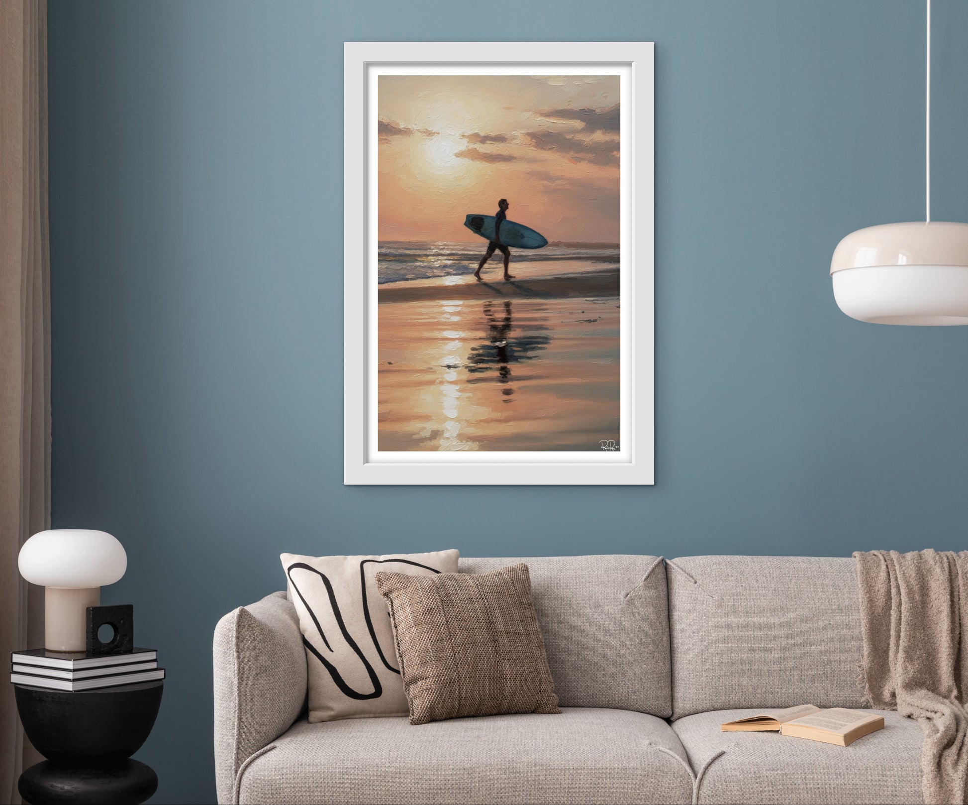 Framed artwork of a person with a surfboard at sunset on a wall above a sofa.