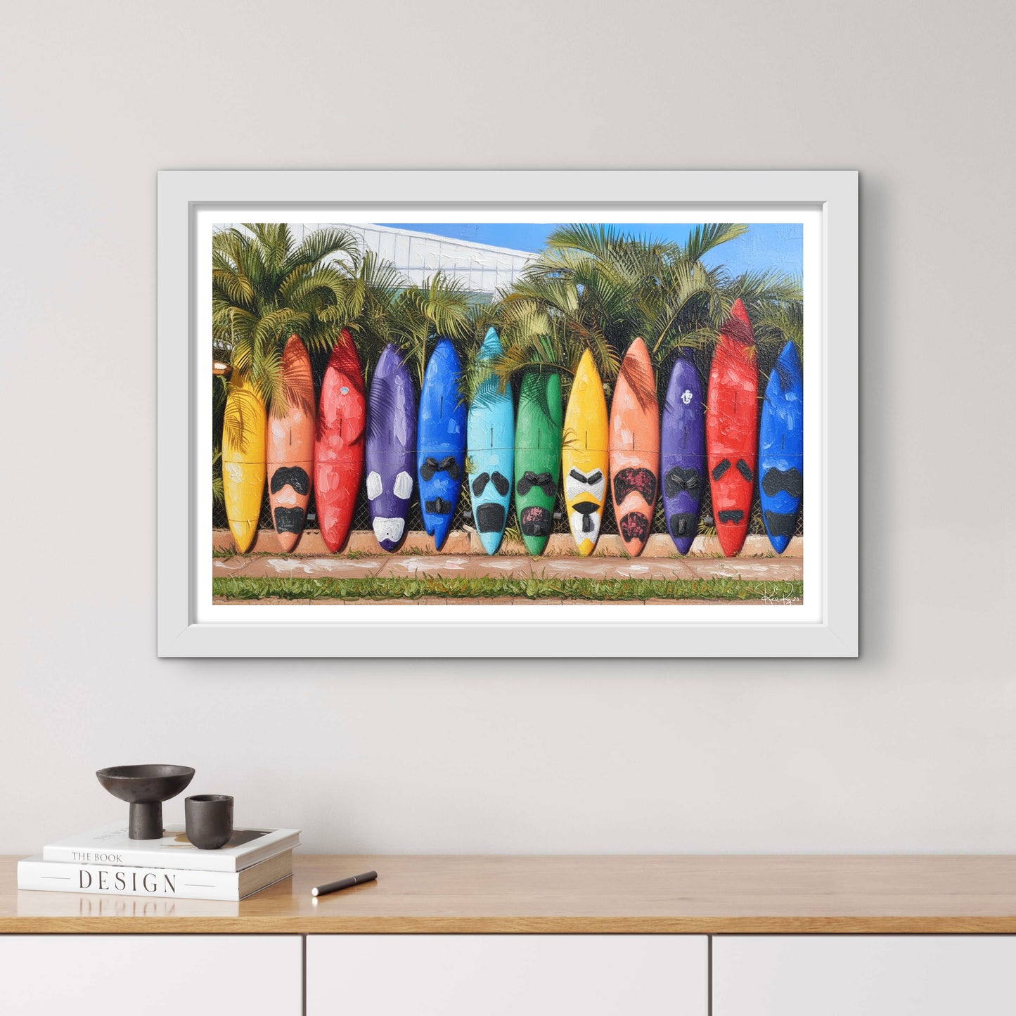 Framed artwork of colorful kayaks against a palm tree background on a wall above a wooden shelf.