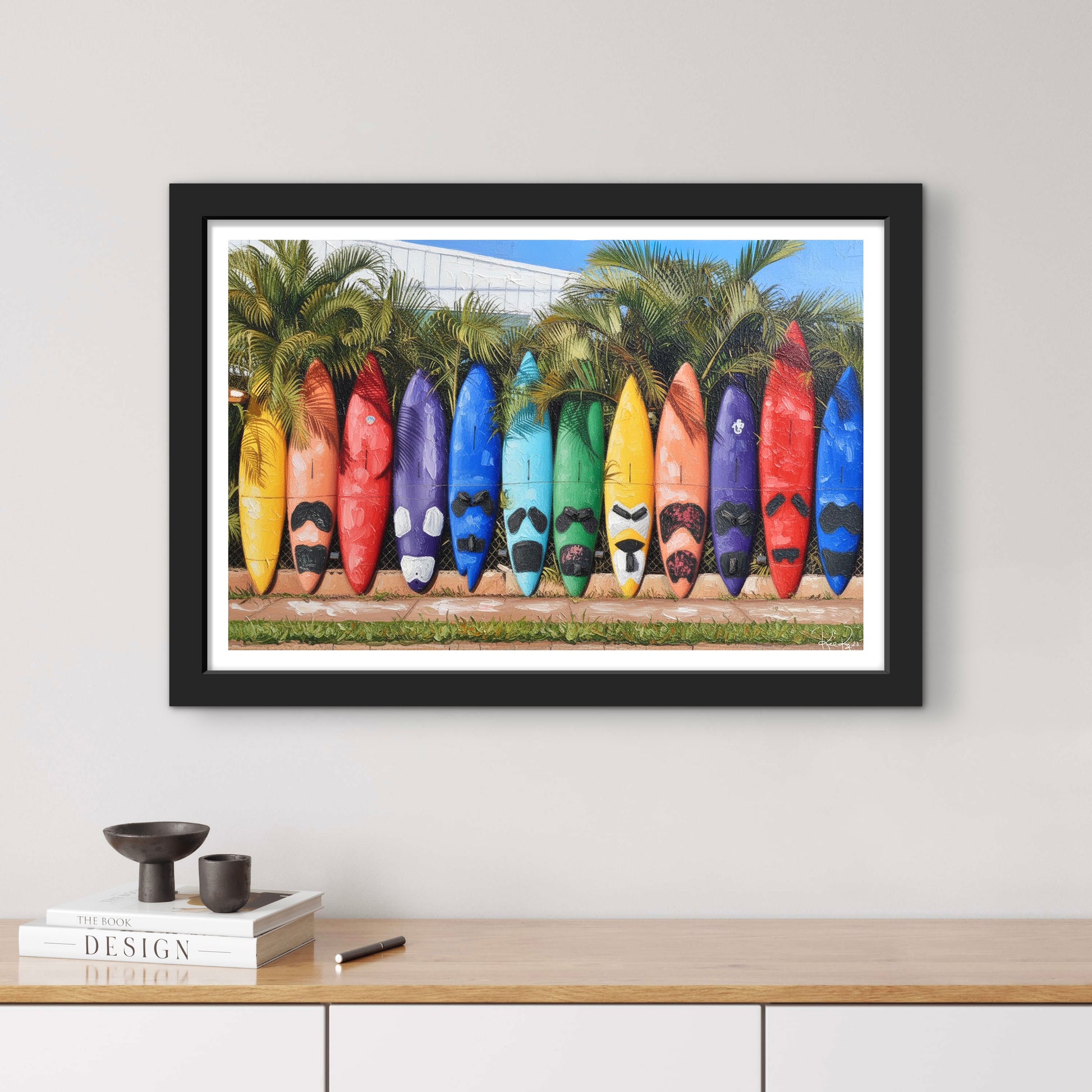 Framed artwork of colorful kayaks against a palm tree background on a wall above a wooden shelf.