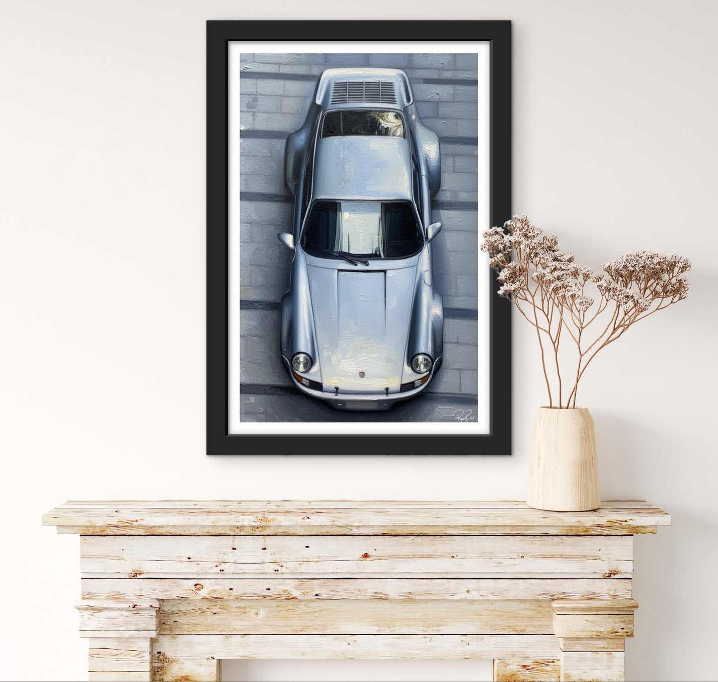 Framed artwork of a vintage car on a white wall above a wooden console table.