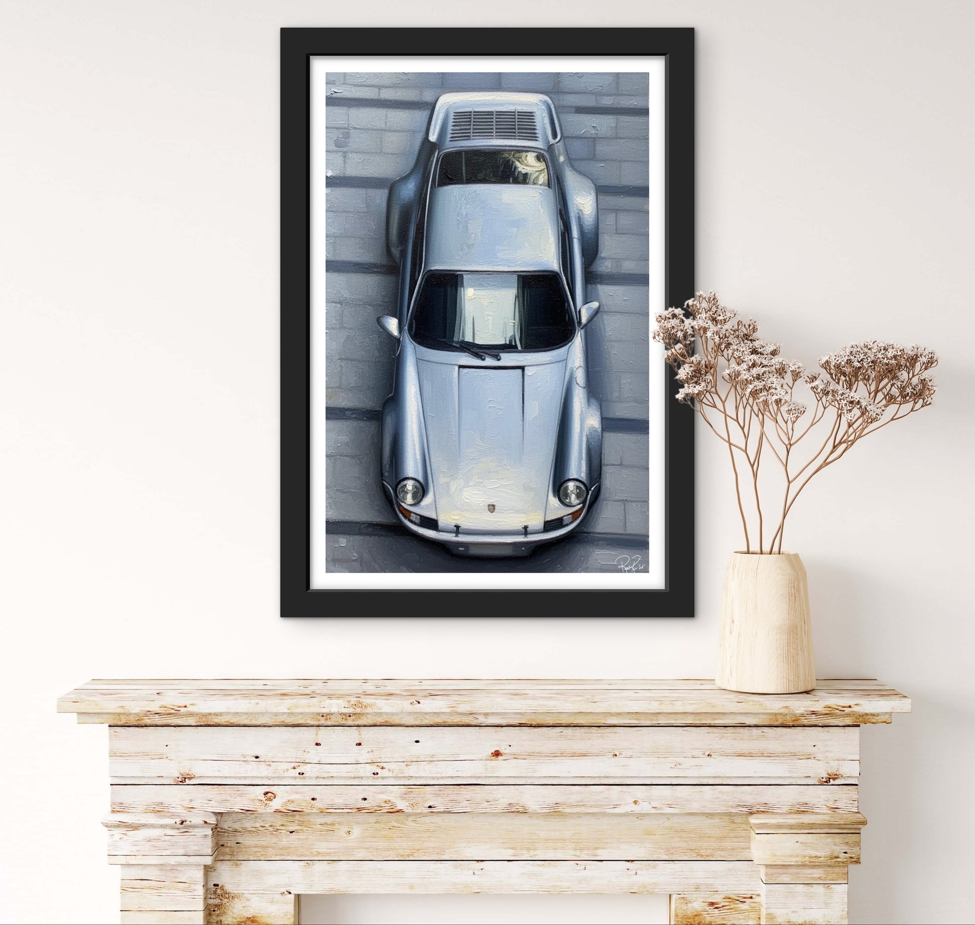 Framed artwork of a vintage car on a white wall above a wooden console table.