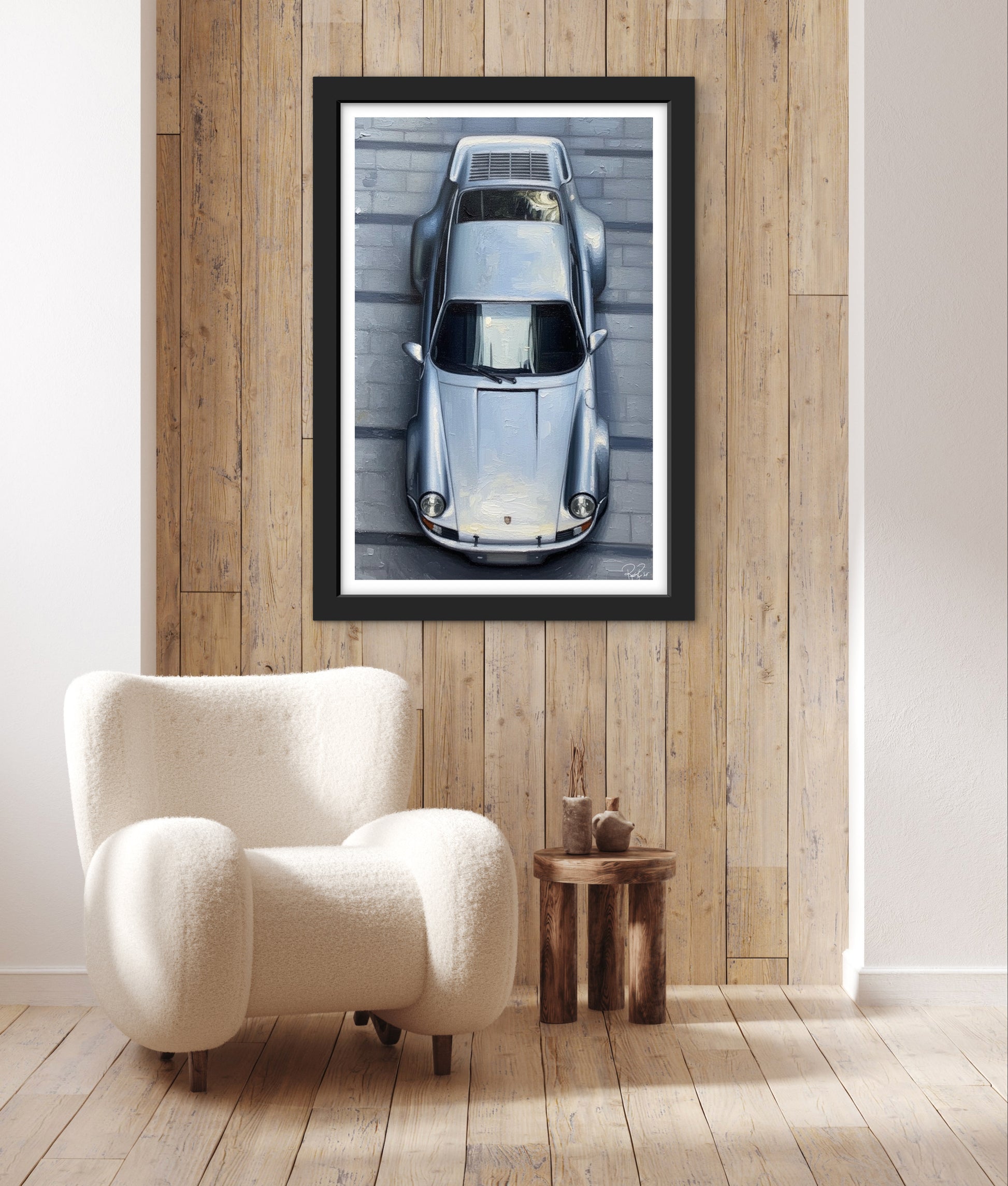 Framed artwork of a car on a wooden wall above a white armchair.